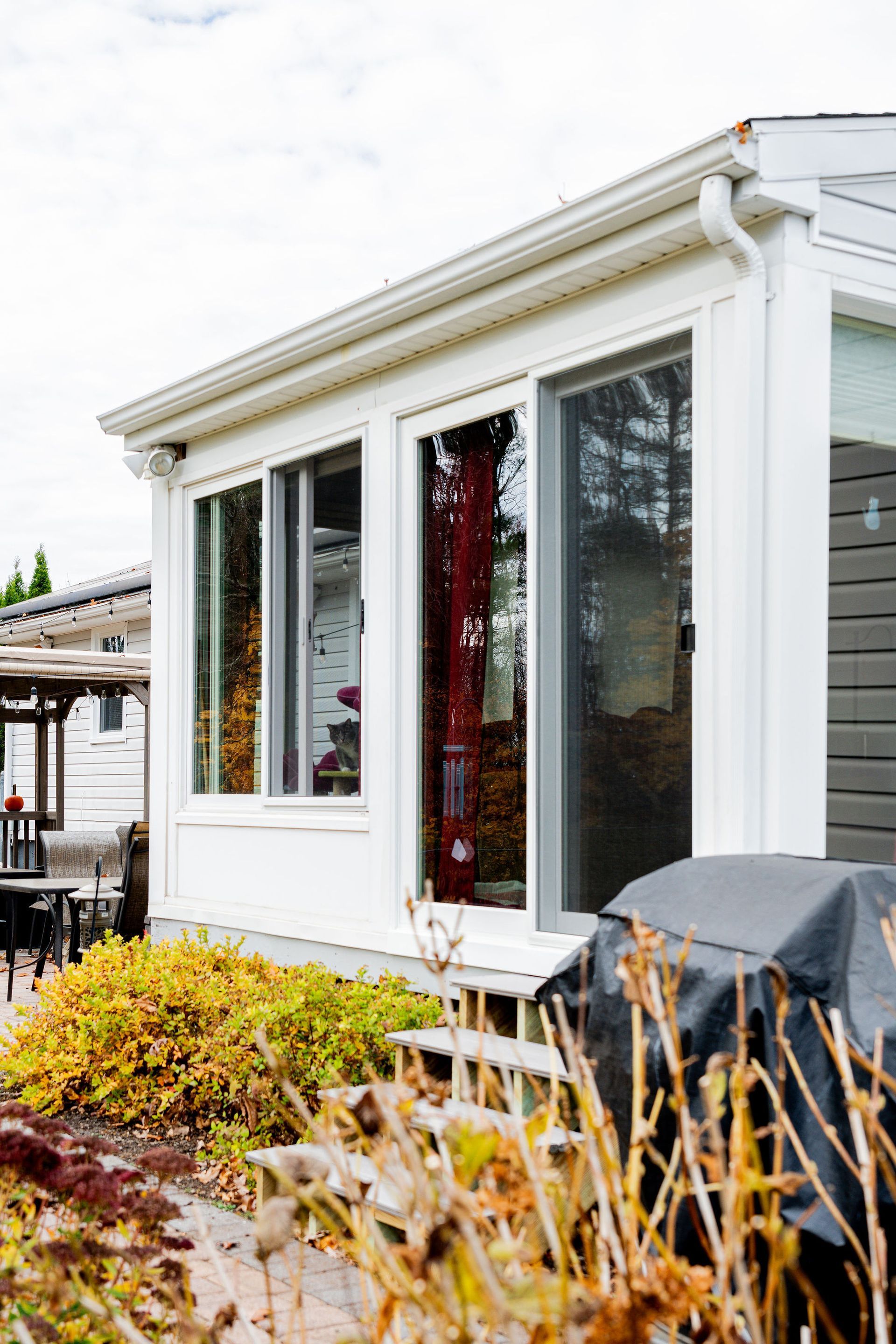 White sunroom with glass windows, a partially open sliding door, and outdoor plants.