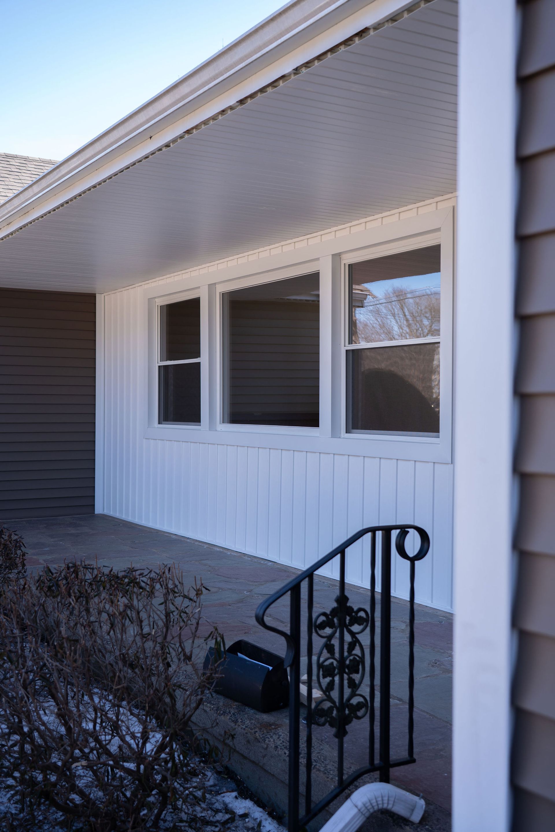 Front porch with white siding, windows, and a black railing. Gray porch.