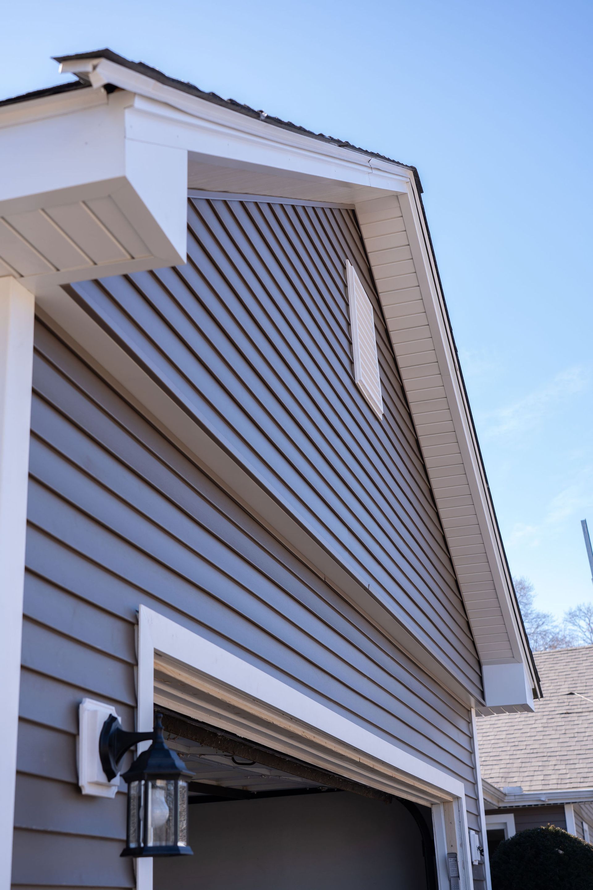 Garage exterior with blue-gray siding, white trim, and open garage door under a clear blue sky.