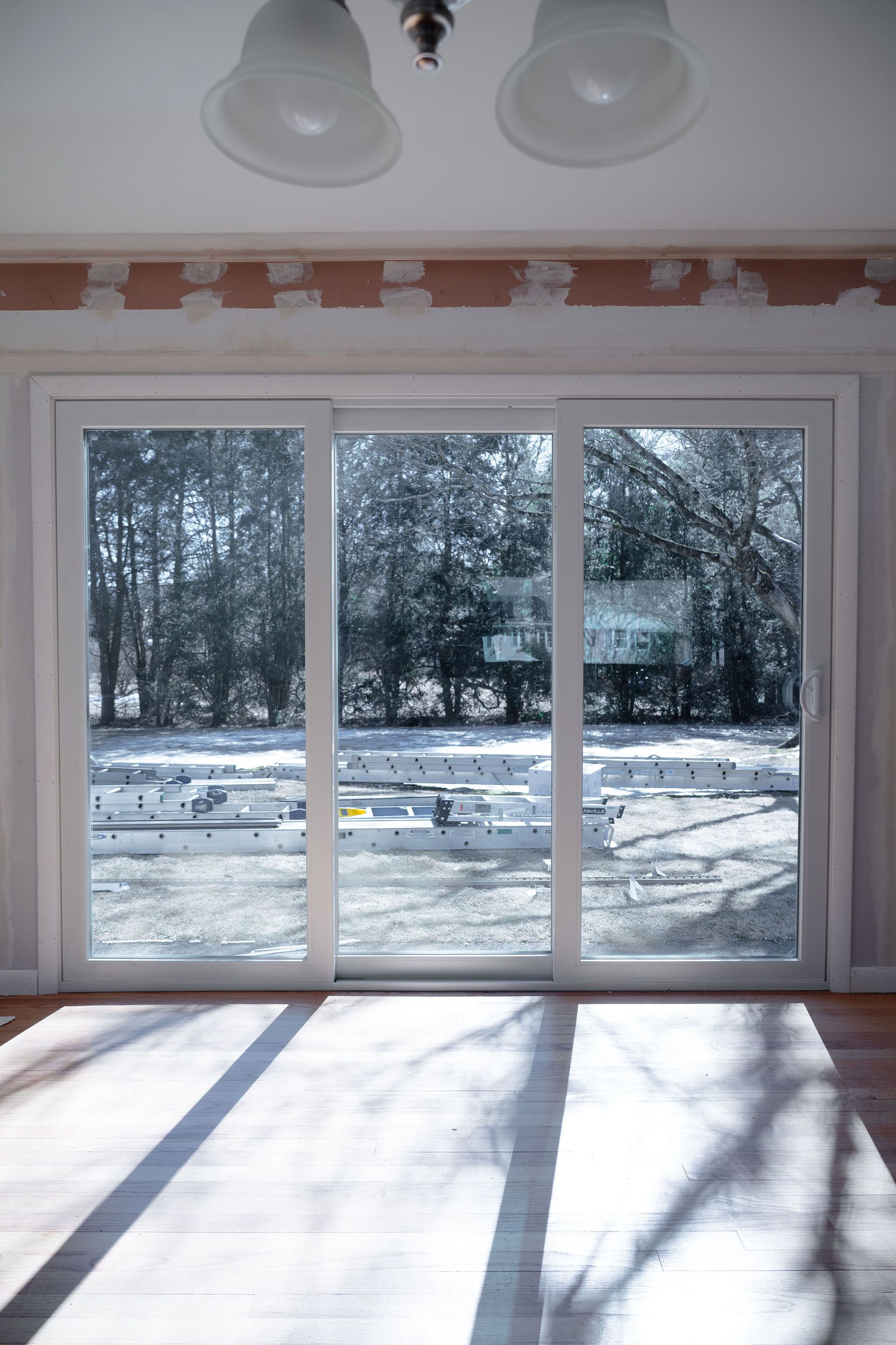 Sliding glass door in a room with hardwood floor and a view of a snowy backyard and trees.
