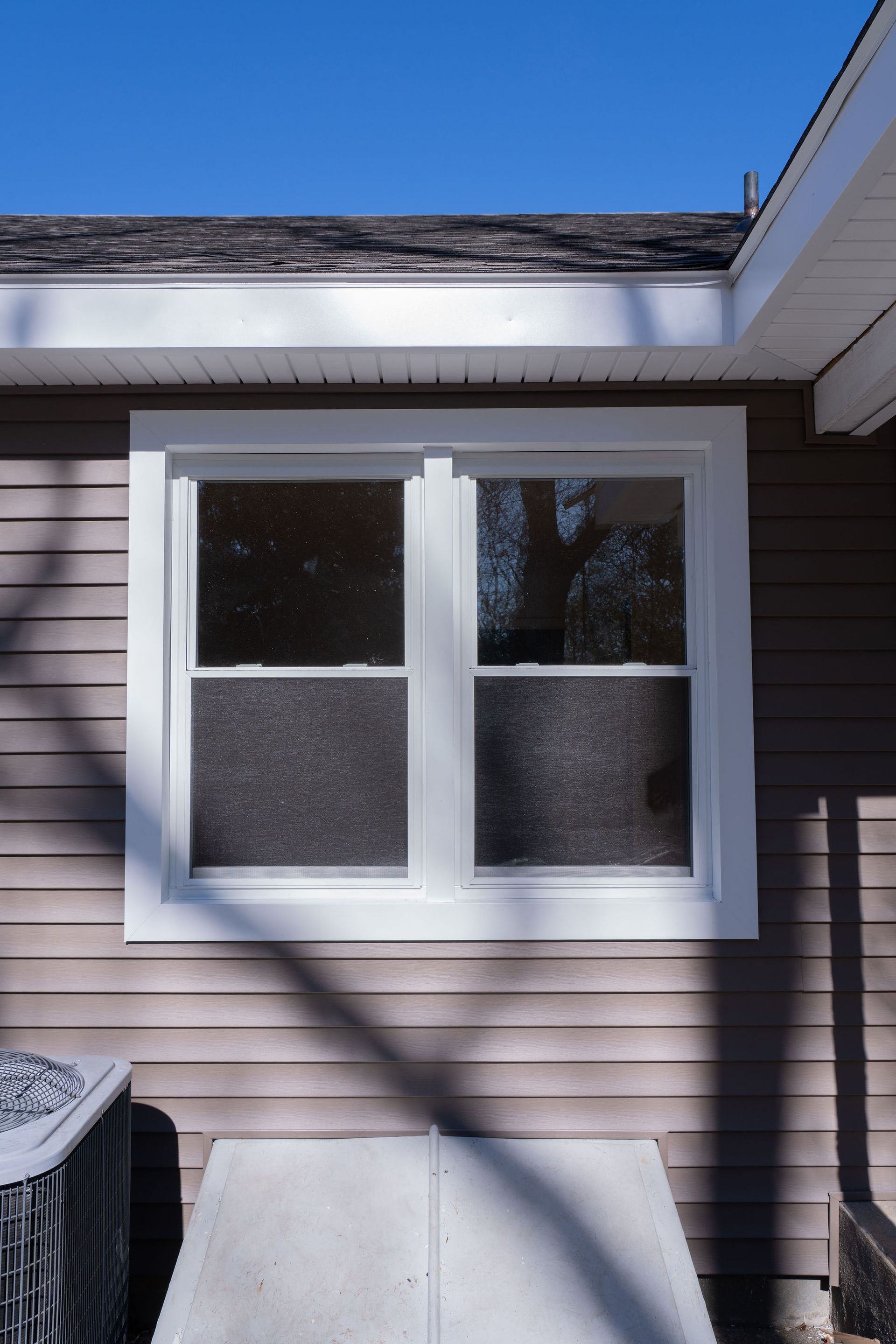 White-framed window on a brown-sided building with a dark gray roof, beneath a clear blue sky.