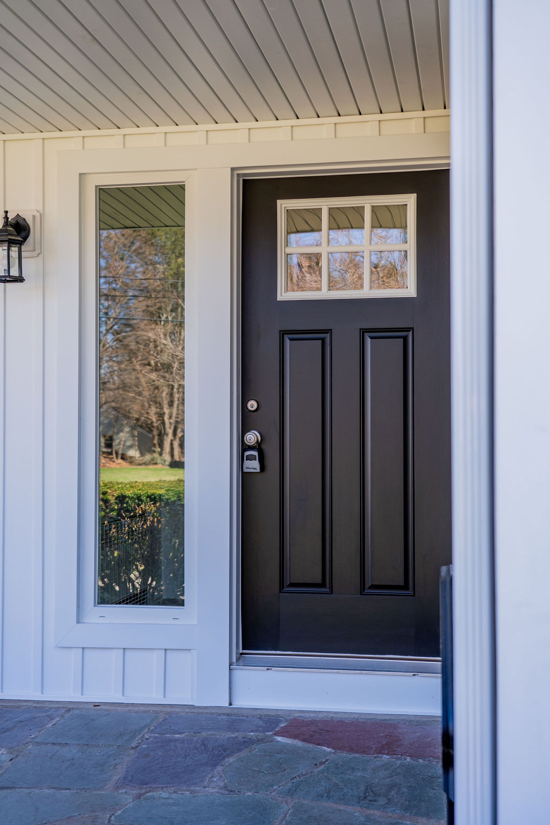 Black front door with sidelight, white trim, and a porch.