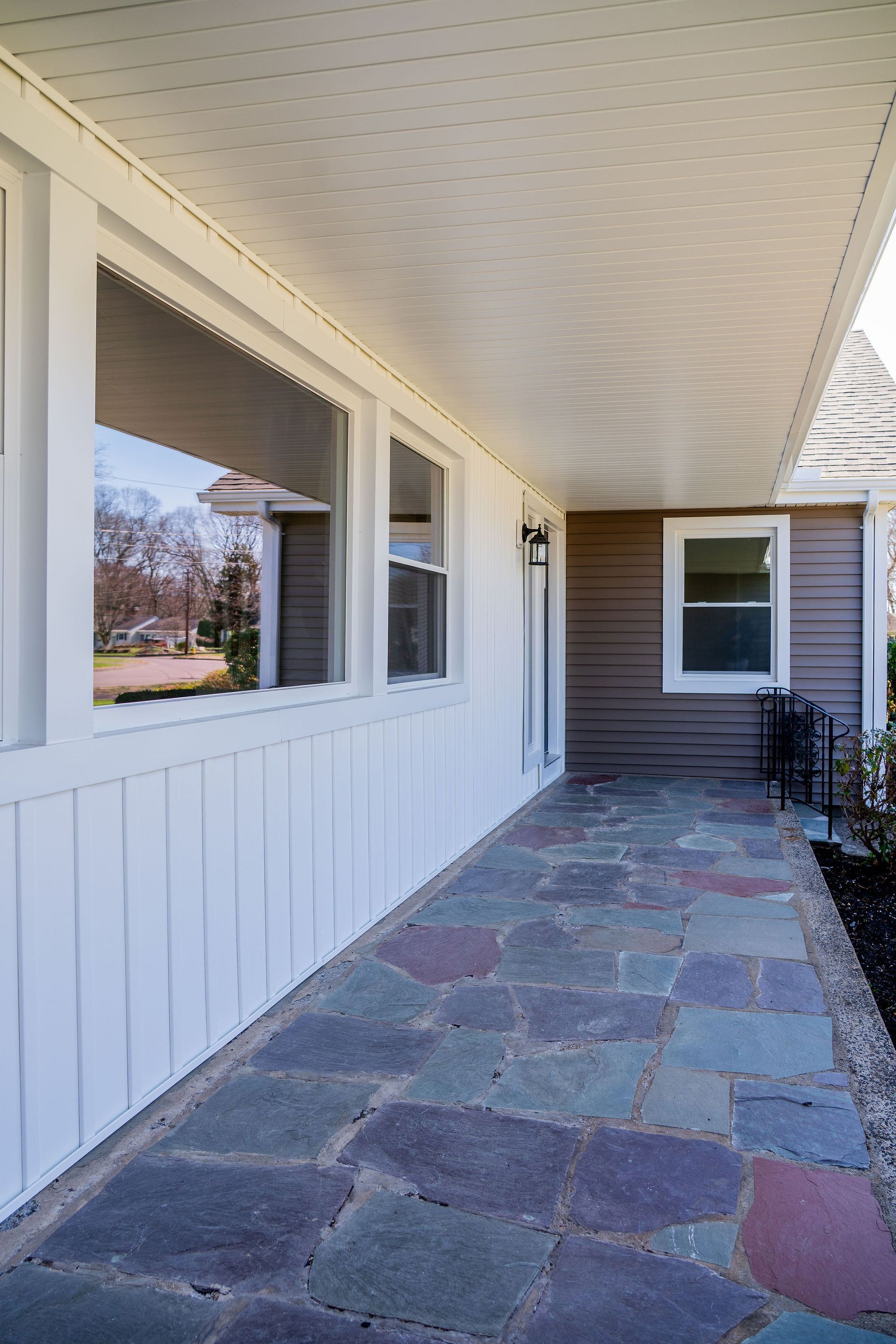 Covered porch with flagstone path, white siding, and windows. Brown exterior wall visible.