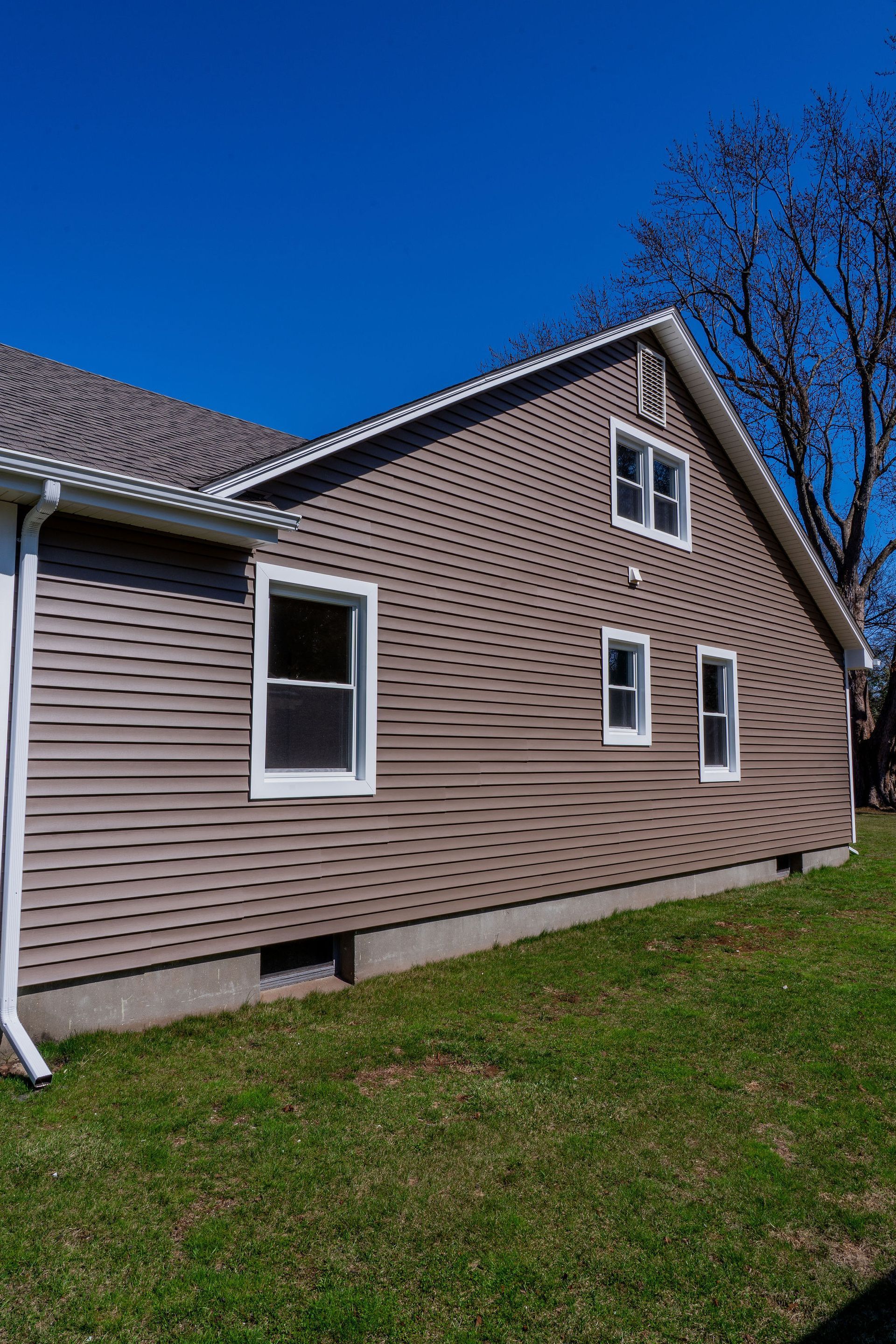 Side view of a brown house with white trim and windows under a bright blue sky.