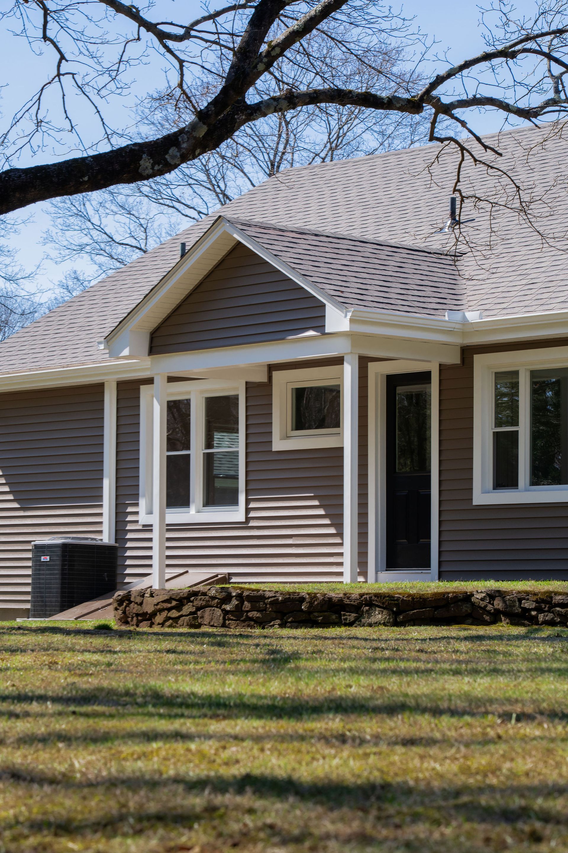 Tan house with white trim and a black door, viewed from a grassy yard.