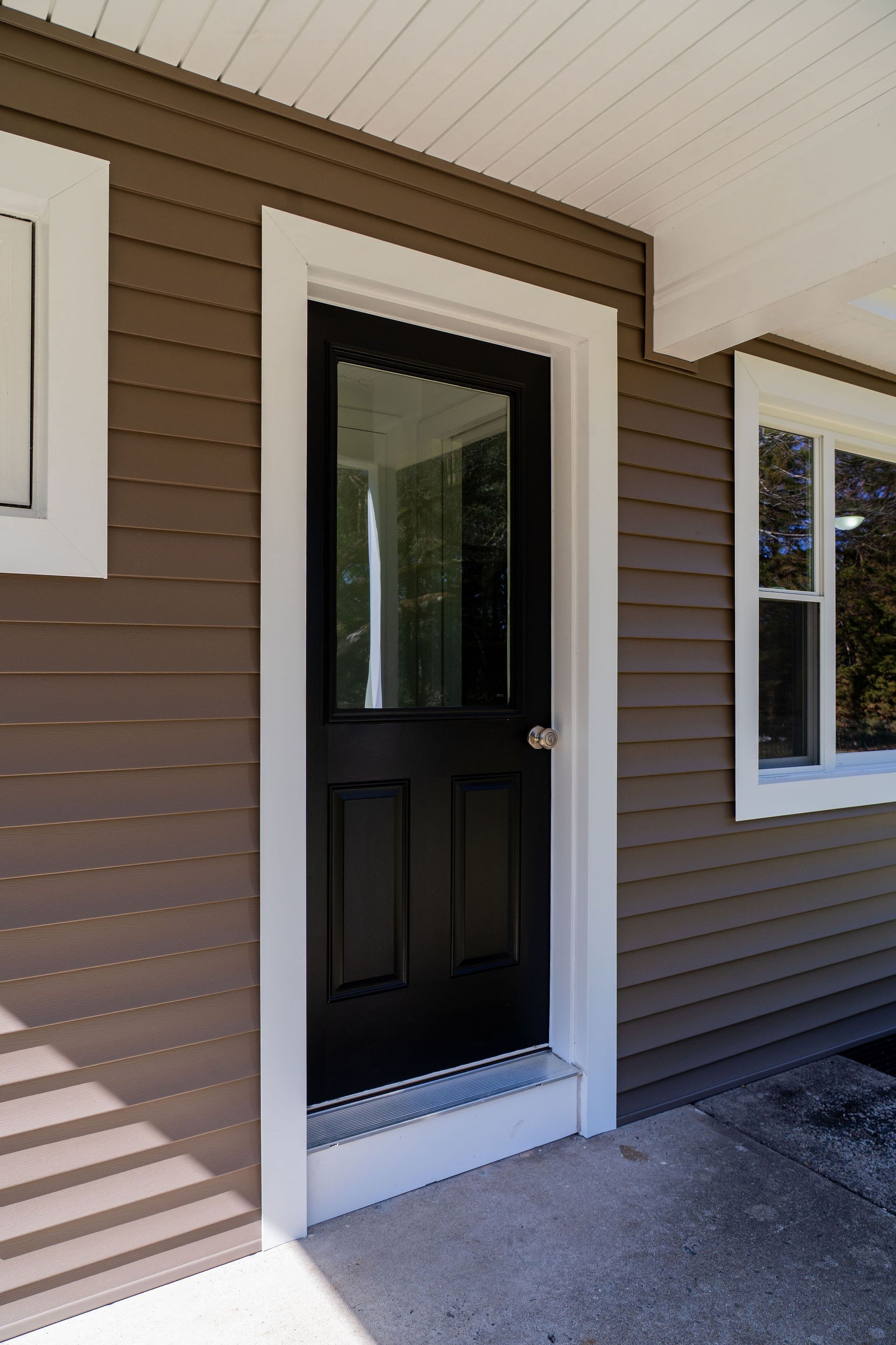 Black front door with glass panel and white trim, on brown siding exterior.