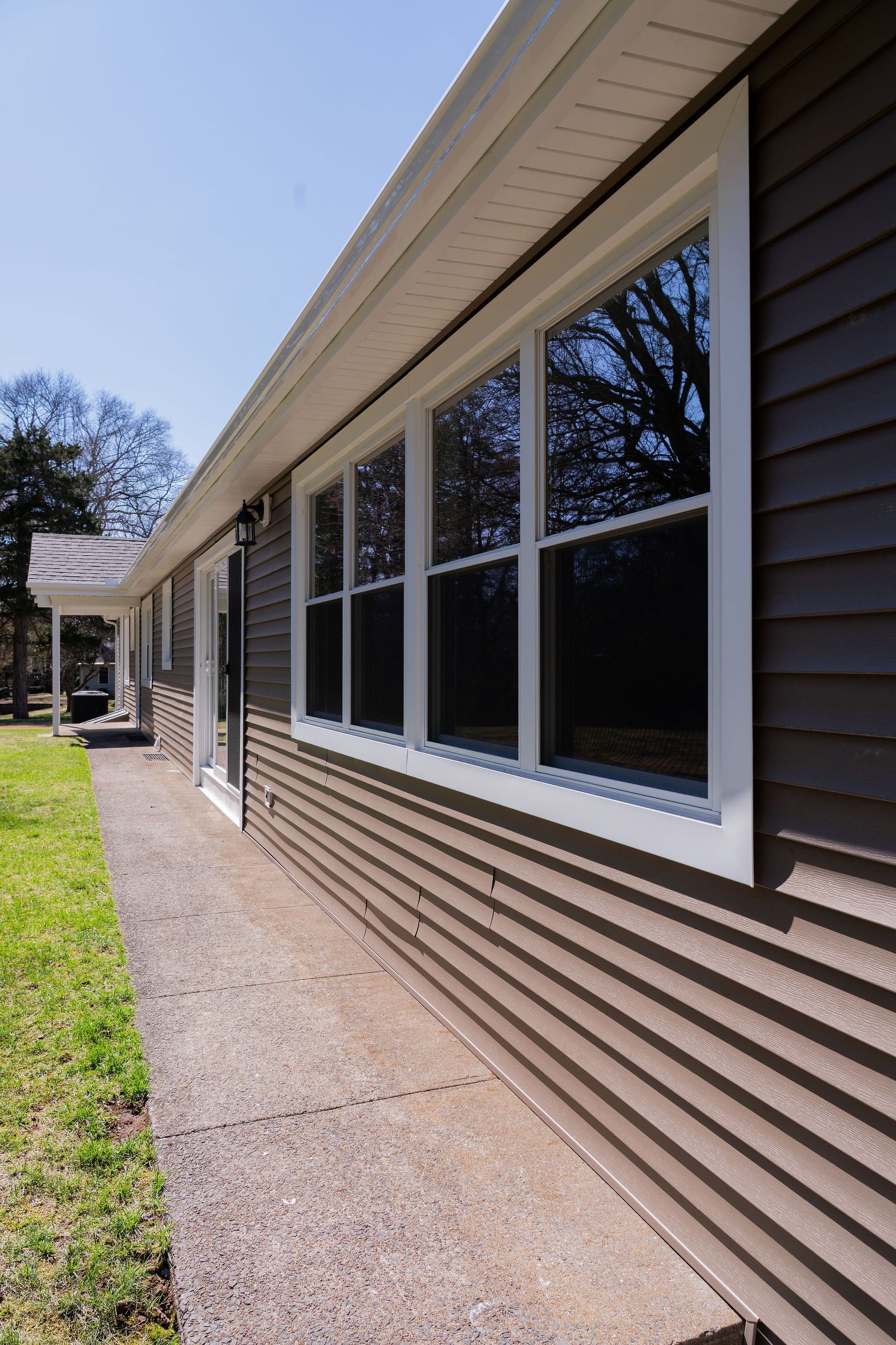 Side view of a house with brown siding, white windows, and a sidewalk.