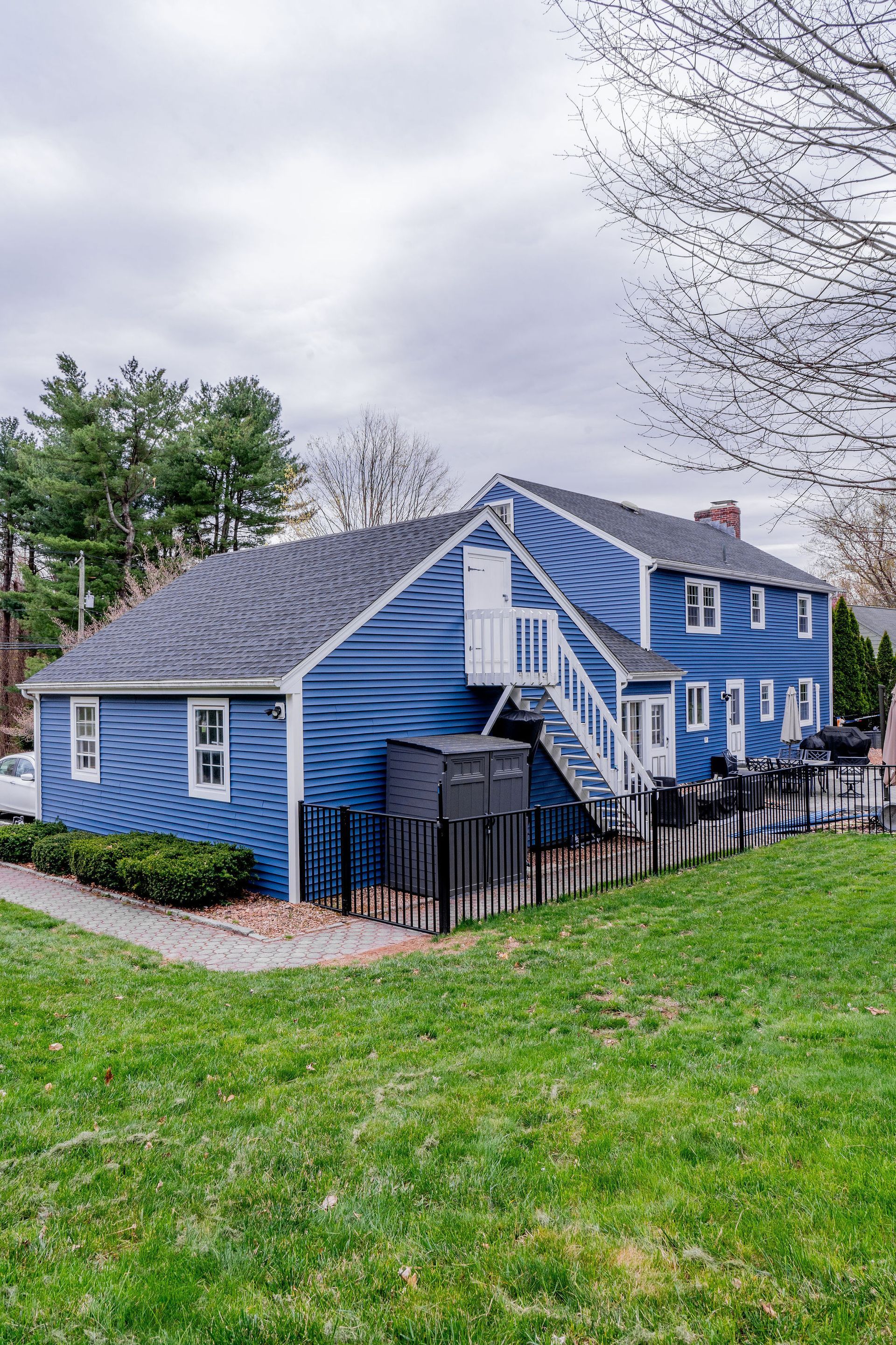 Blue house with white trim and exterior stairs, behind a black fence and green grass.