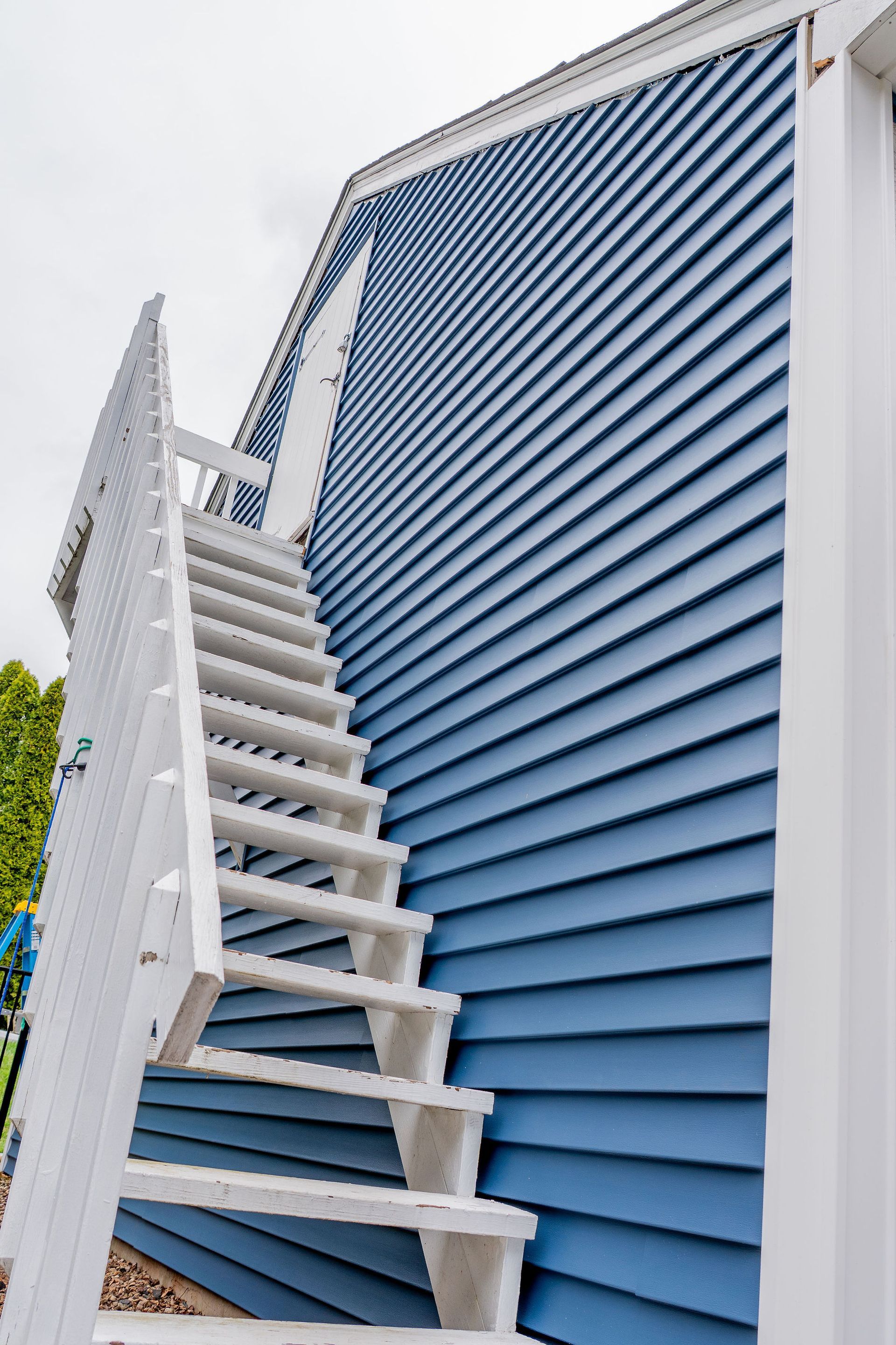 White wooden staircase on blue clapboard siding of a building, ascending upwards.