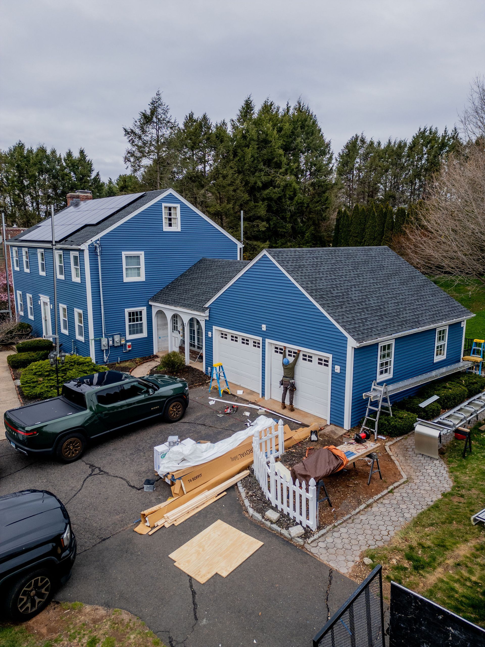 Blue house and garage under construction, with a green pickup truck in the driveway.