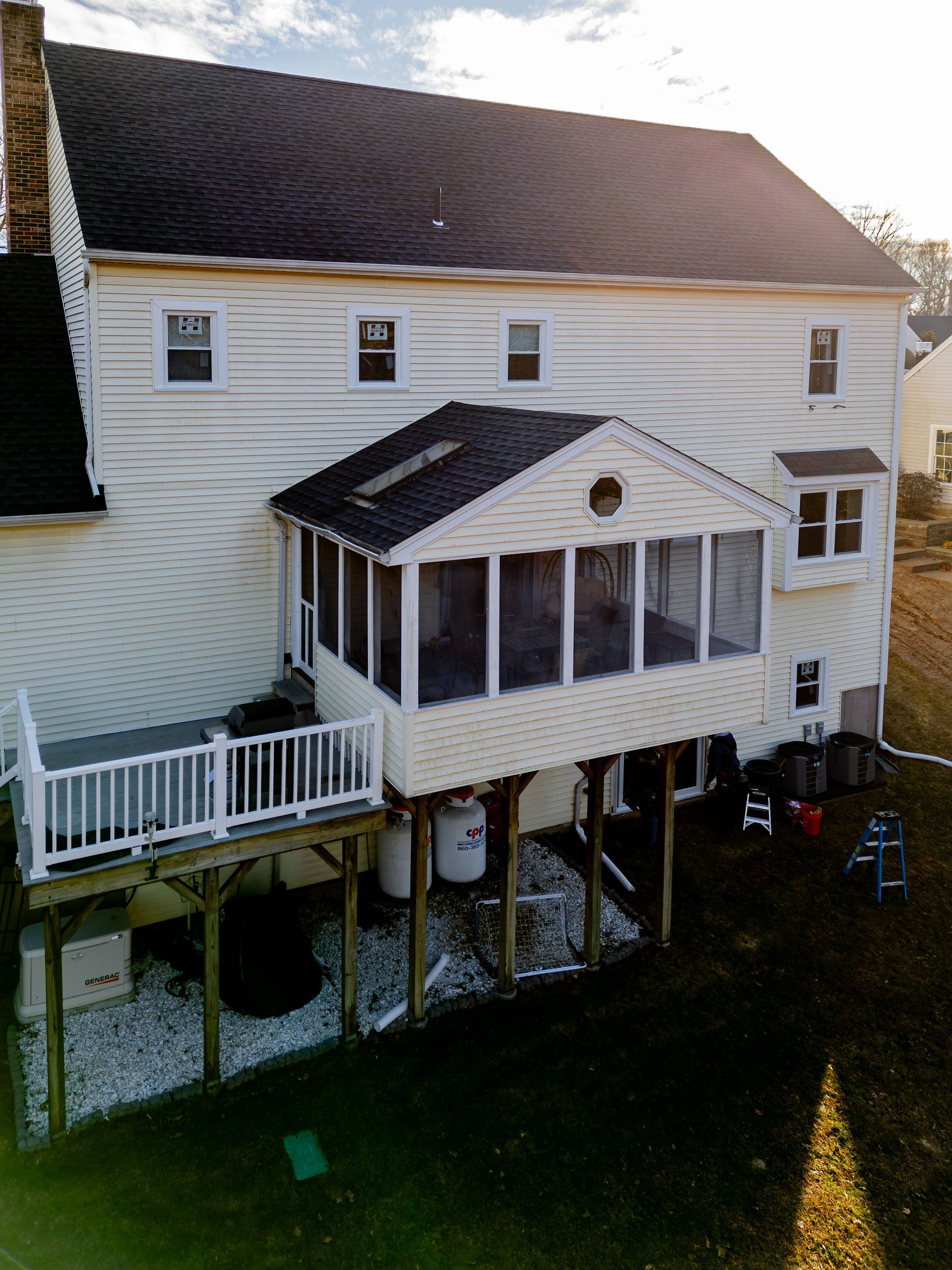 A two-story house with a screened-in porch and deck, surrounded by grass.