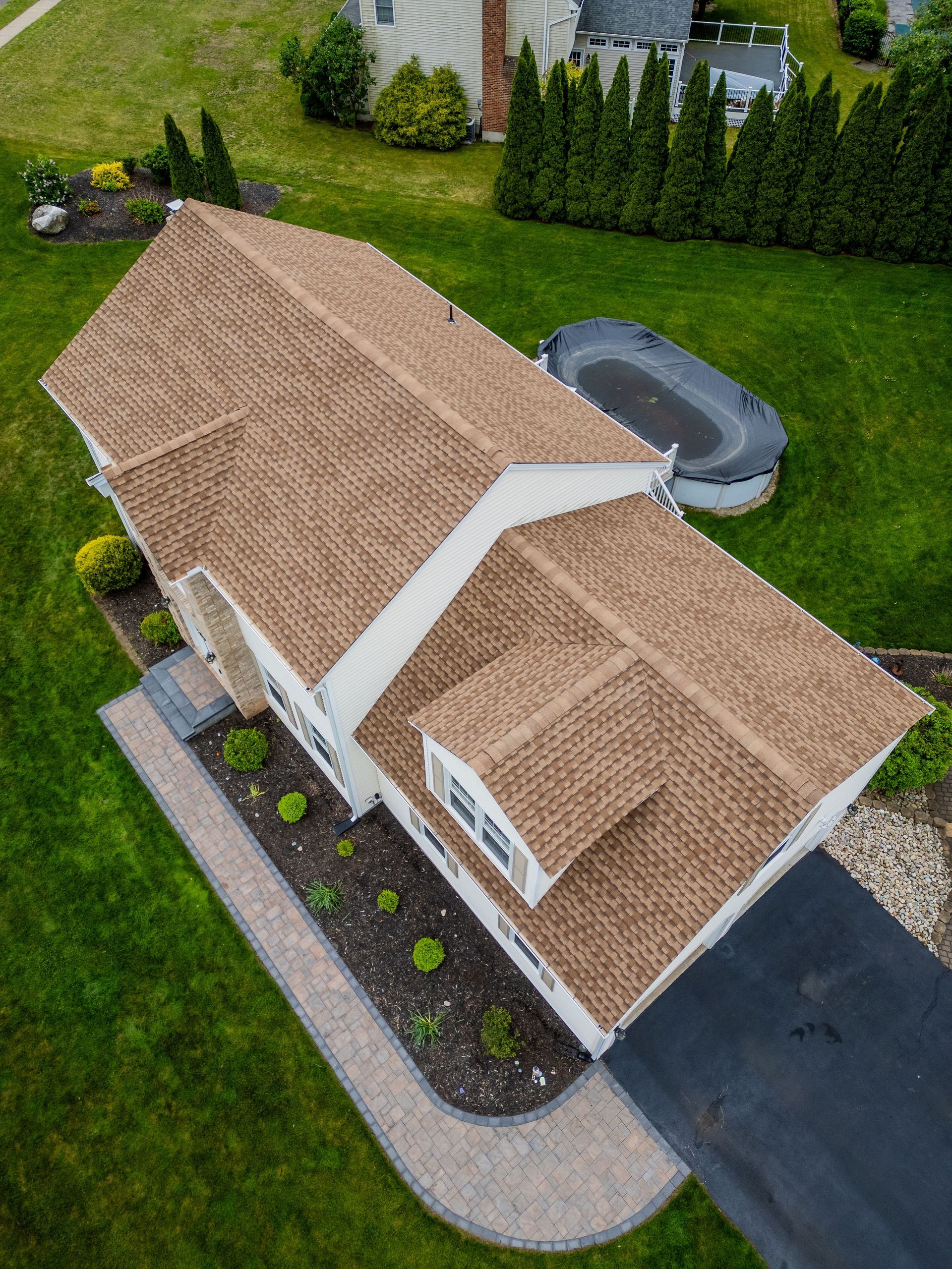 Aerial view of a house with a brown roof, black driveway, and surrounding green lawn.