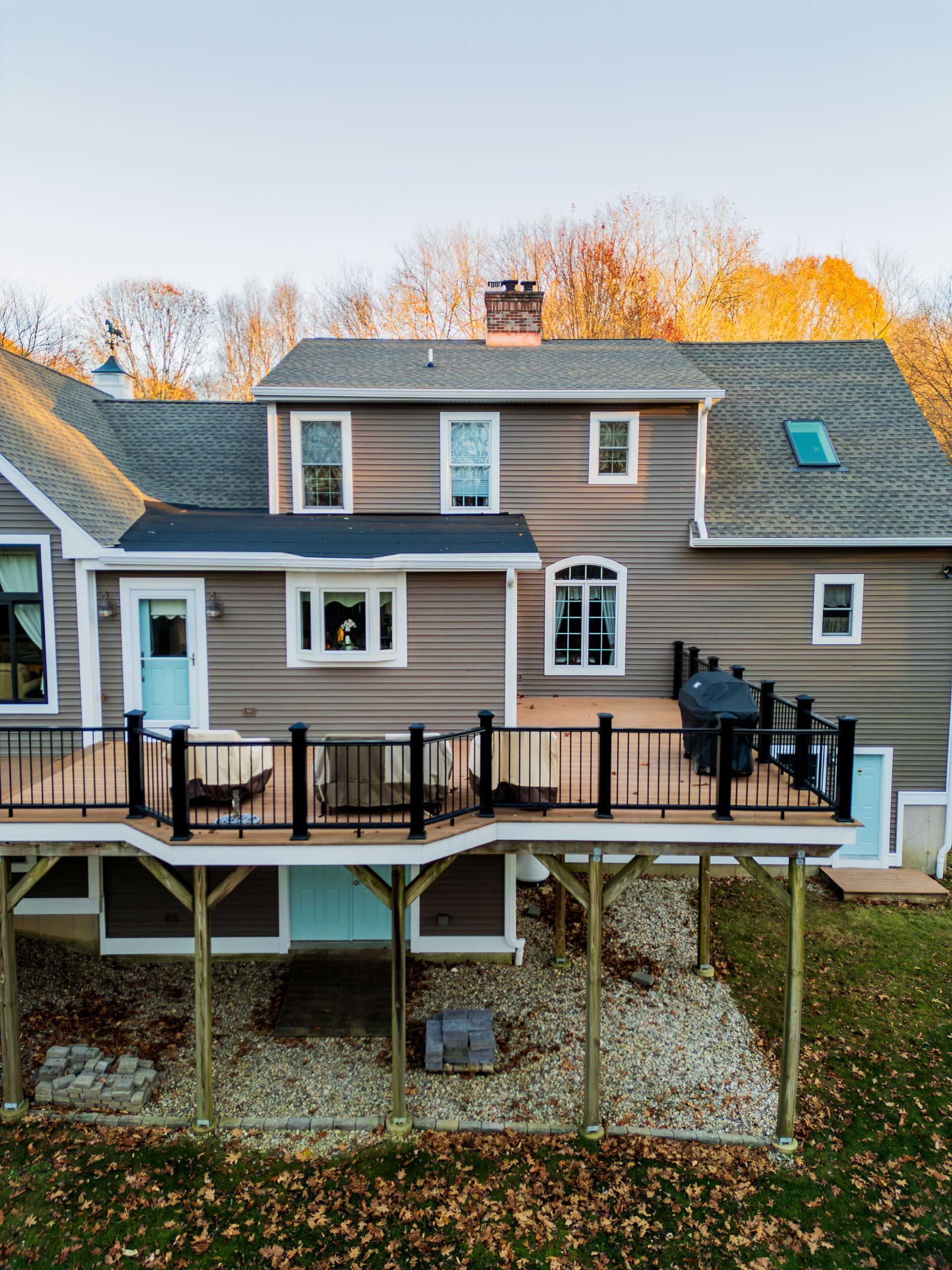 Two-story house with a deck, brown siding, black railing, and light blue door. Deck overlooks a yard with trees.