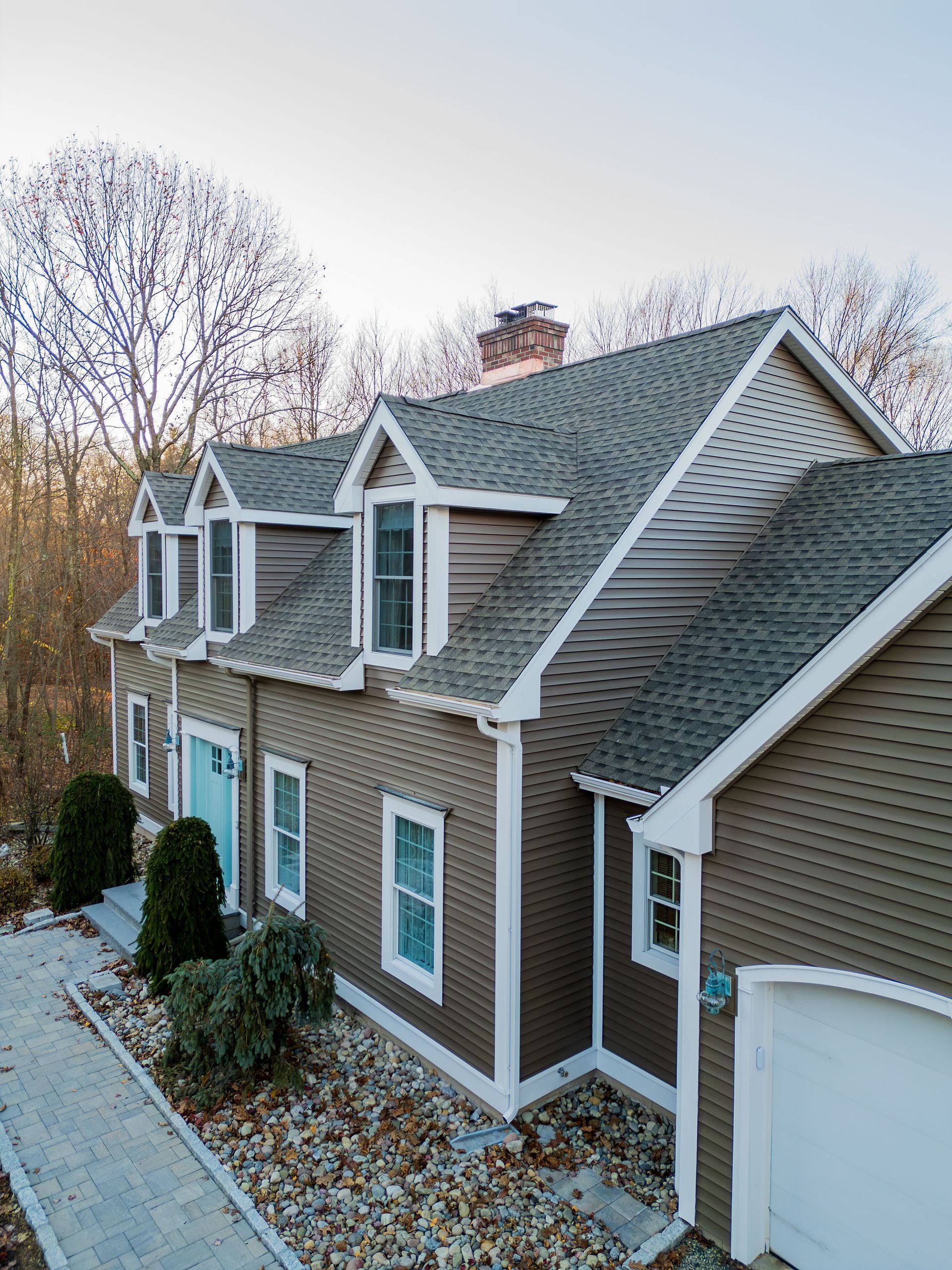 Brown house with white trim, gabled roof, and several windows, near trees.