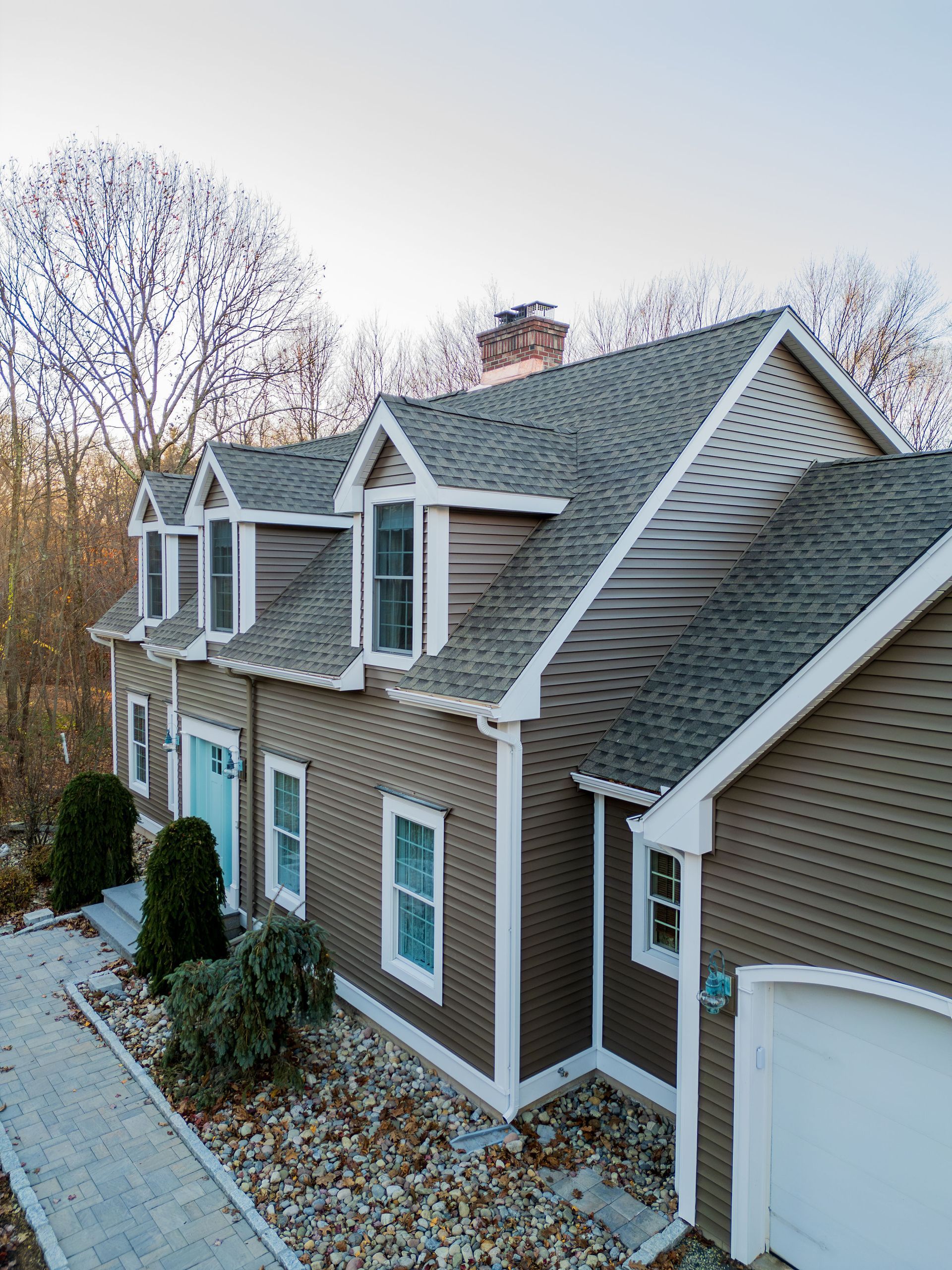 Brown house with three dormers, white trim, and a light blue door.
