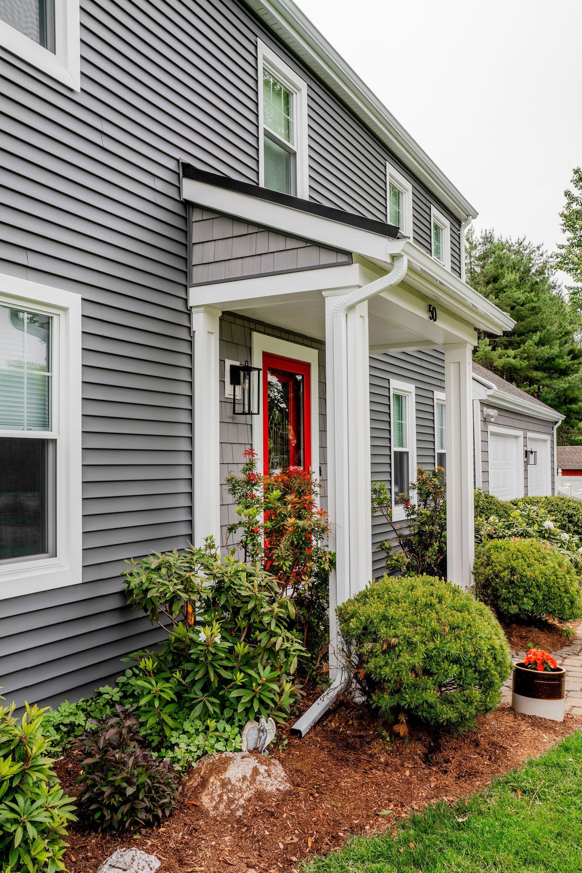Gray house with a red door and white trim; shrubs line the front.