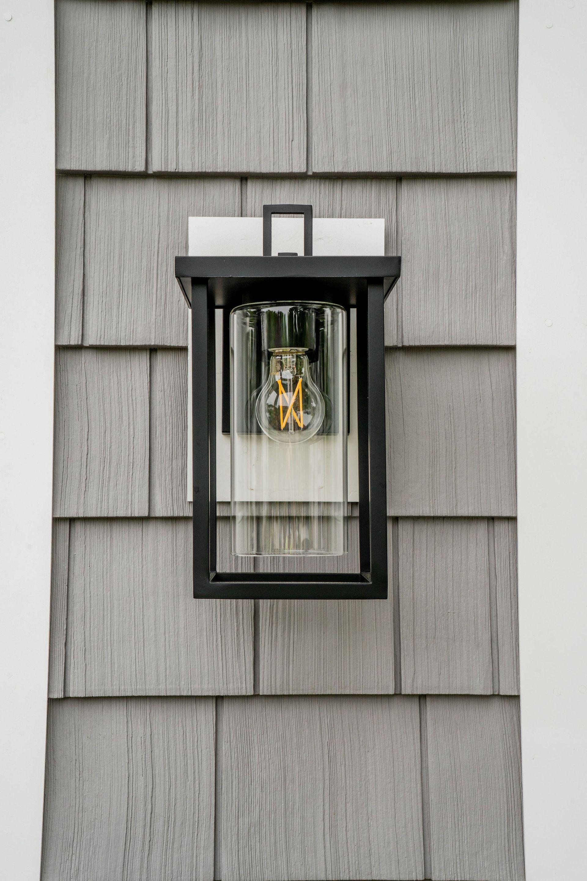 Black outdoor wall lantern on gray shingle siding, with white trim.