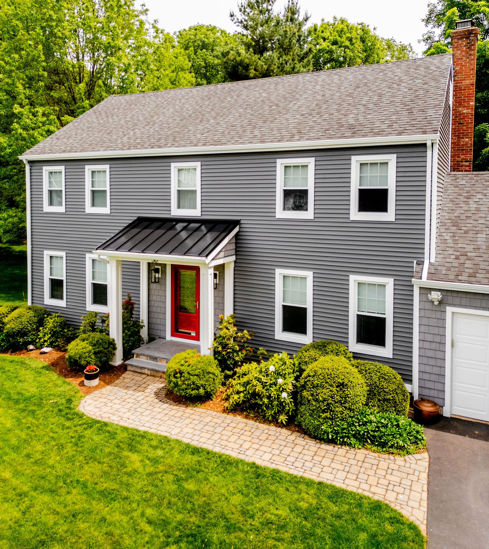 Two-story gray house with red door, black awning, white trim, brick pathway, and green lawn.