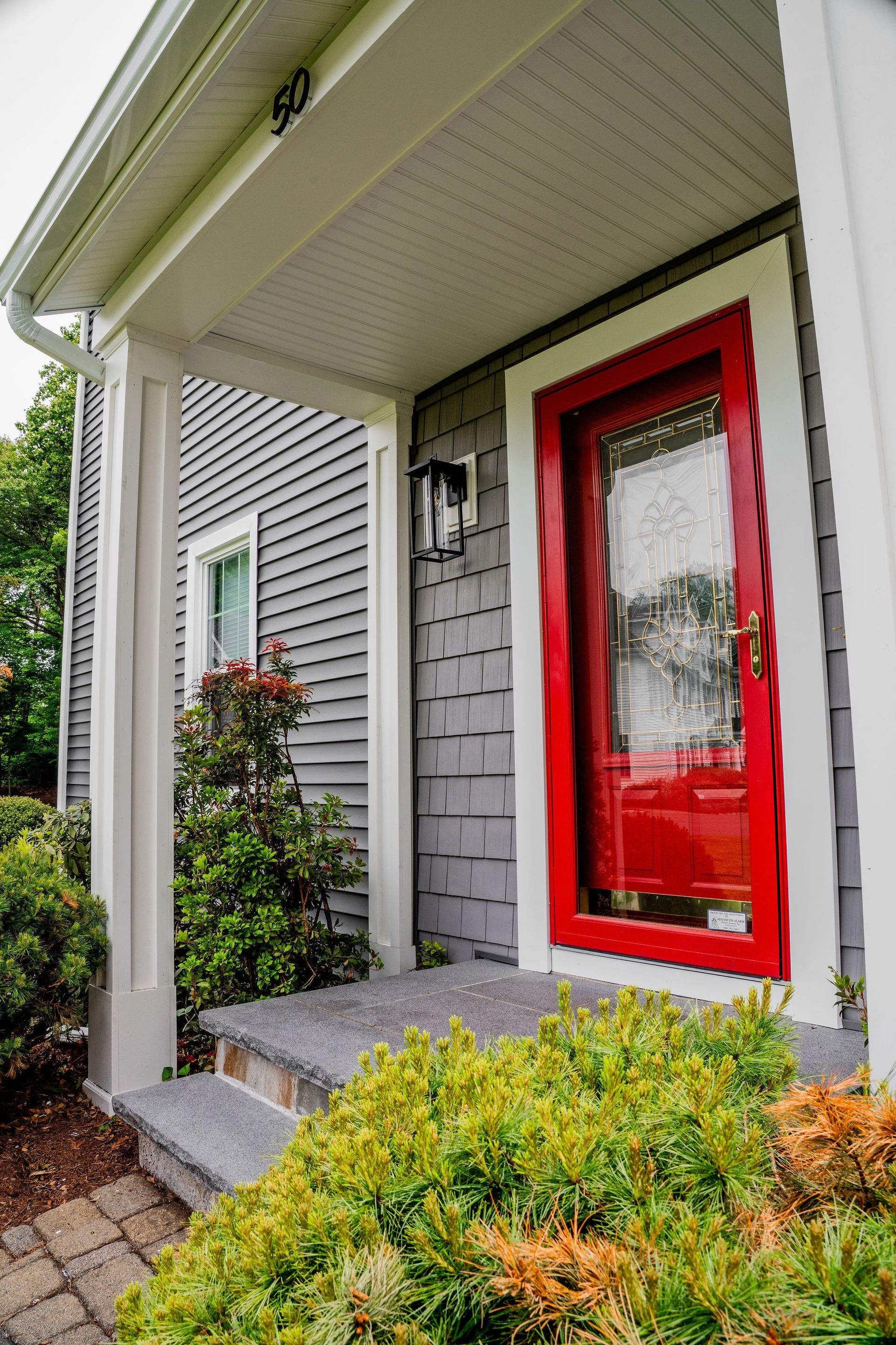 Gray house exterior with red door and white trim; bushes, steps, and porch roof.
