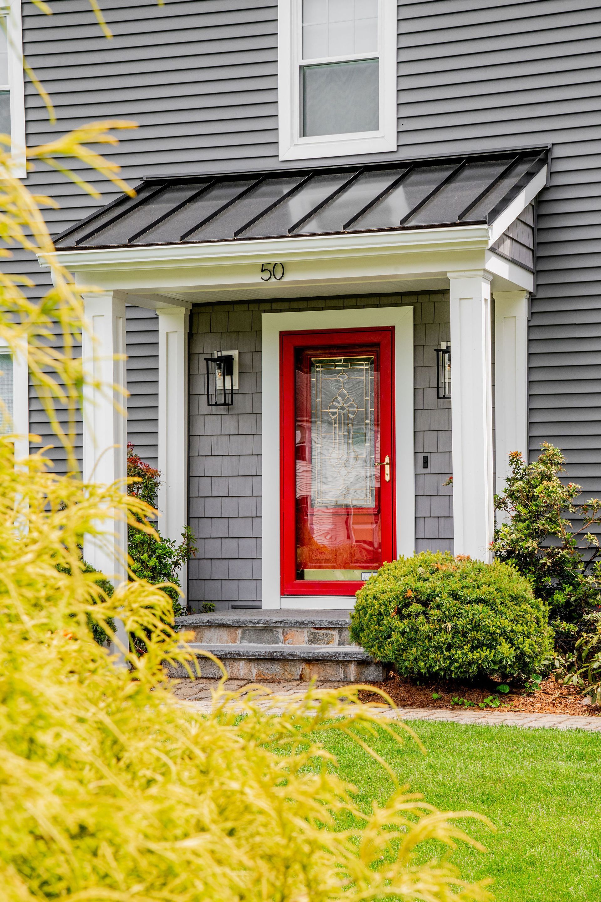 Red front door with glass panel, gray siding, under a black awning.