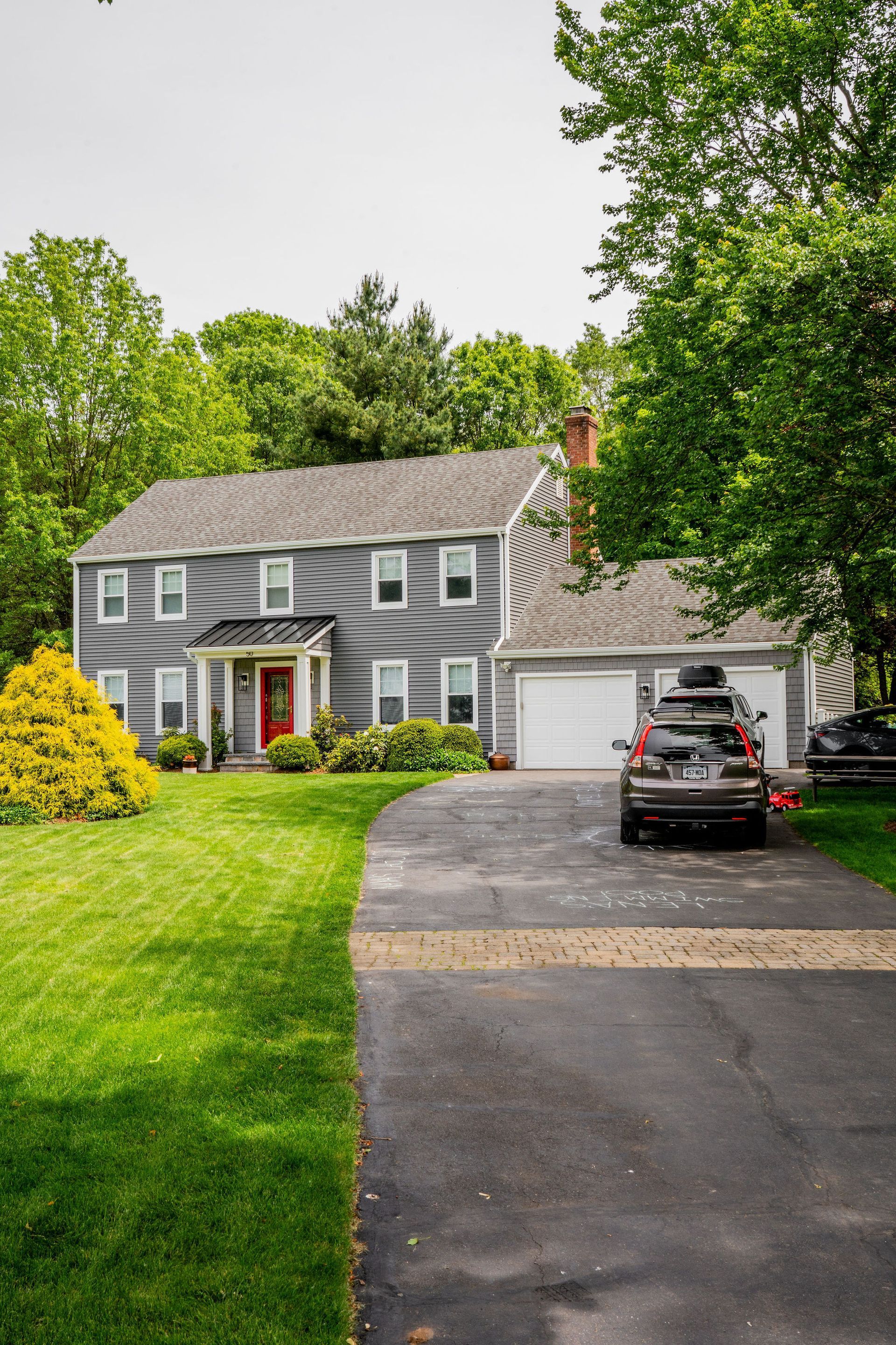 Gray house with green lawn, long driveway, and car parked in front of a two-car garage.