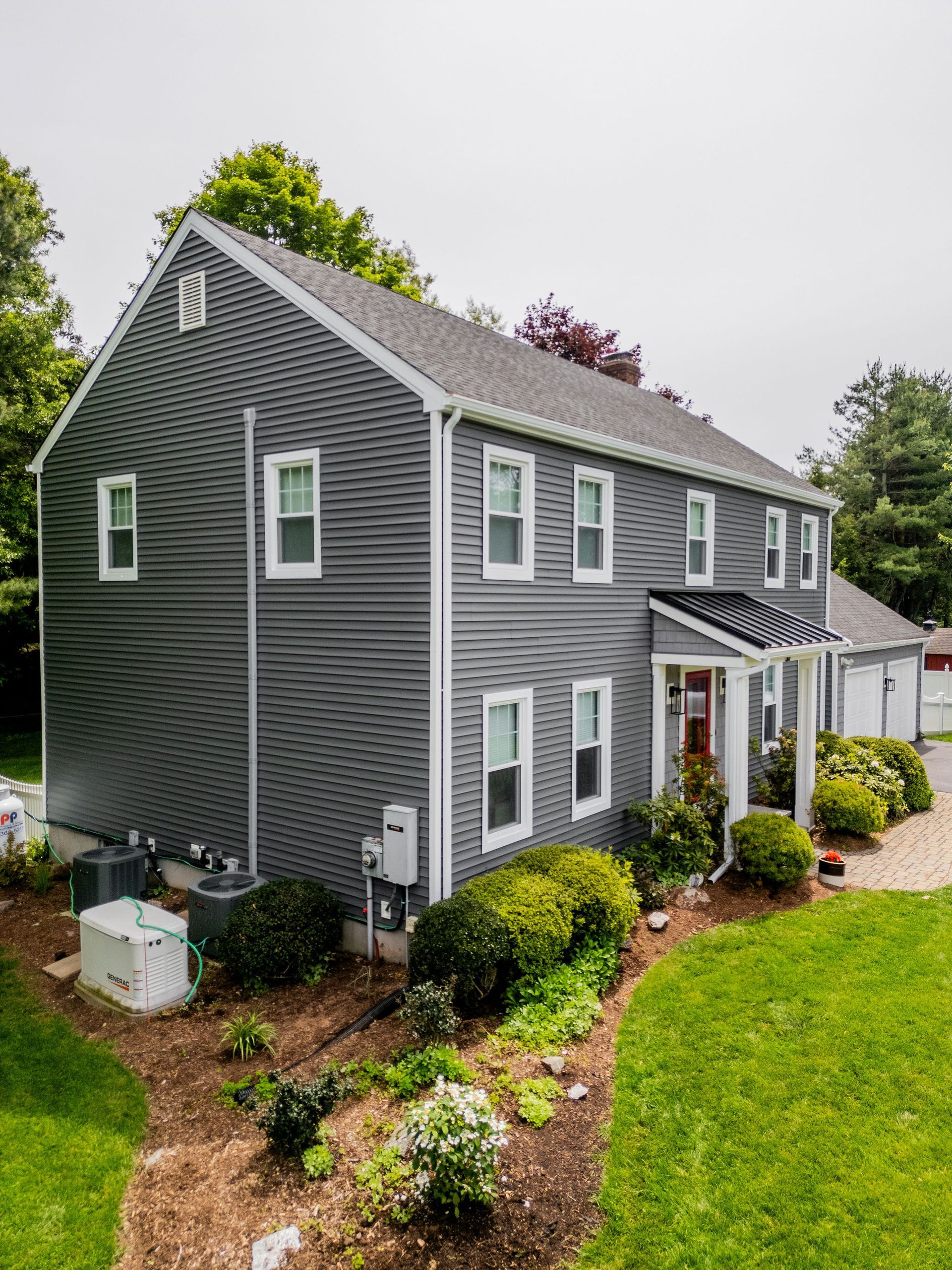 Two-story gray house with white trim, surrounded by a green lawn and garden.