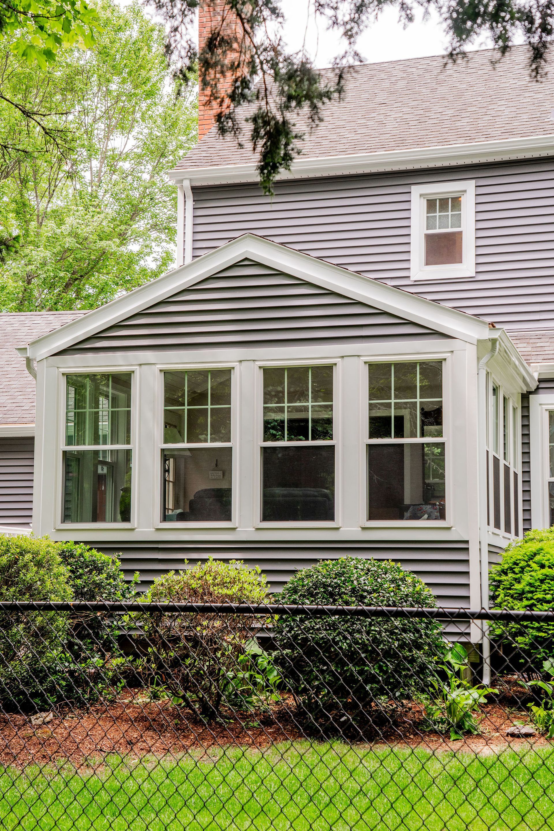 Gray house with white-framed windows, small bushes, and a black fence.