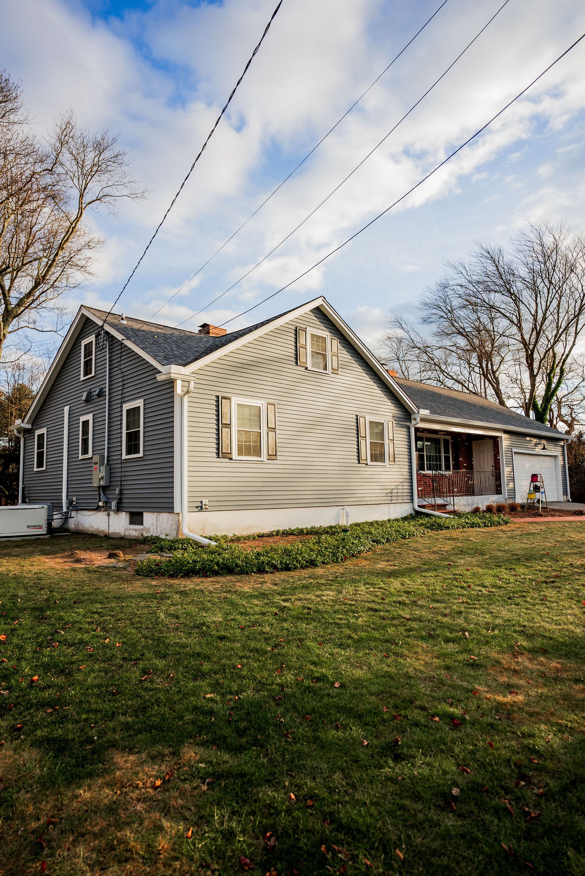 Gray weathered house with overgrown yard, cloudy sky, utility wires.