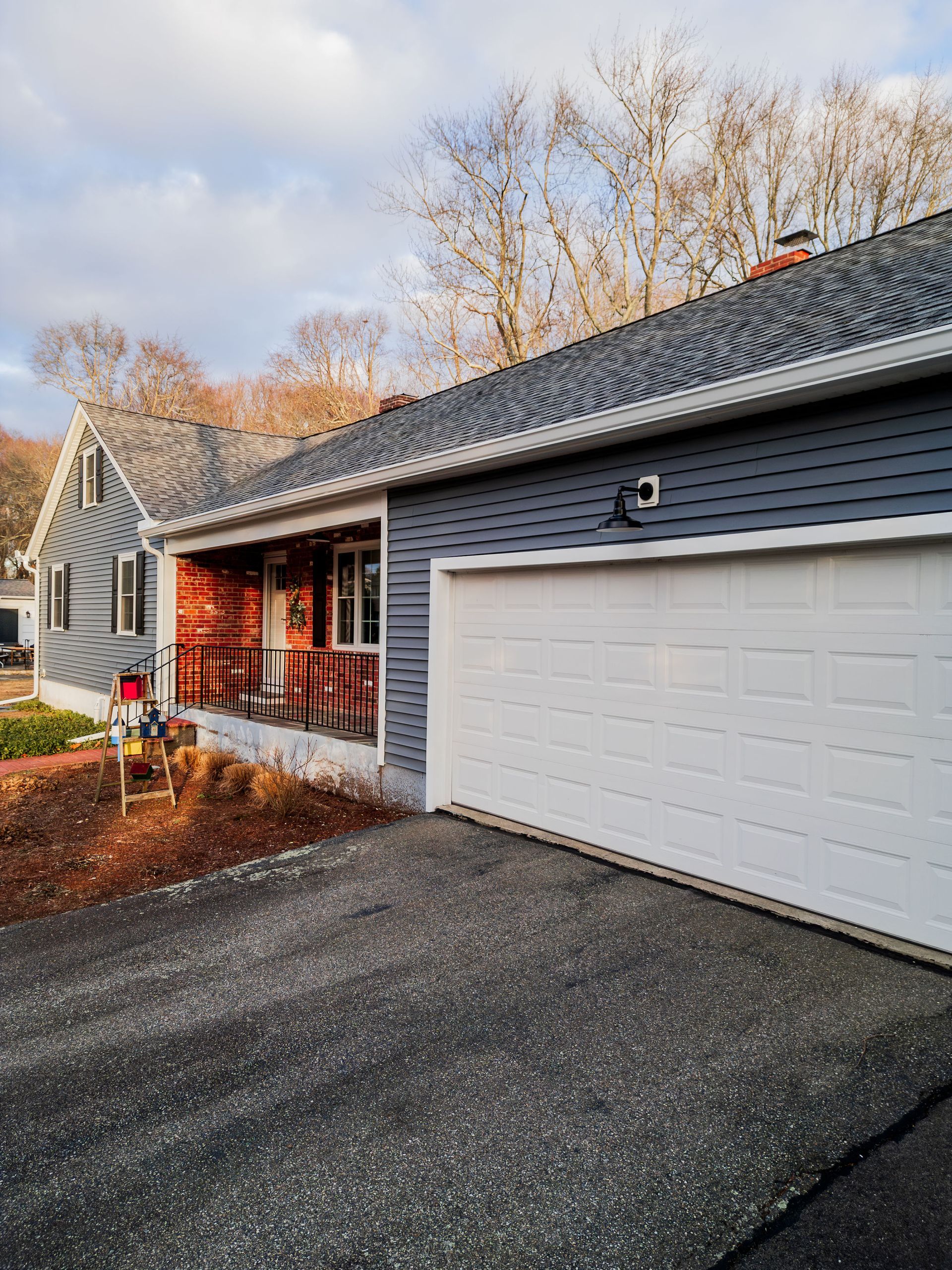 Gray house with white garage door and red porch. Asphalt driveway.