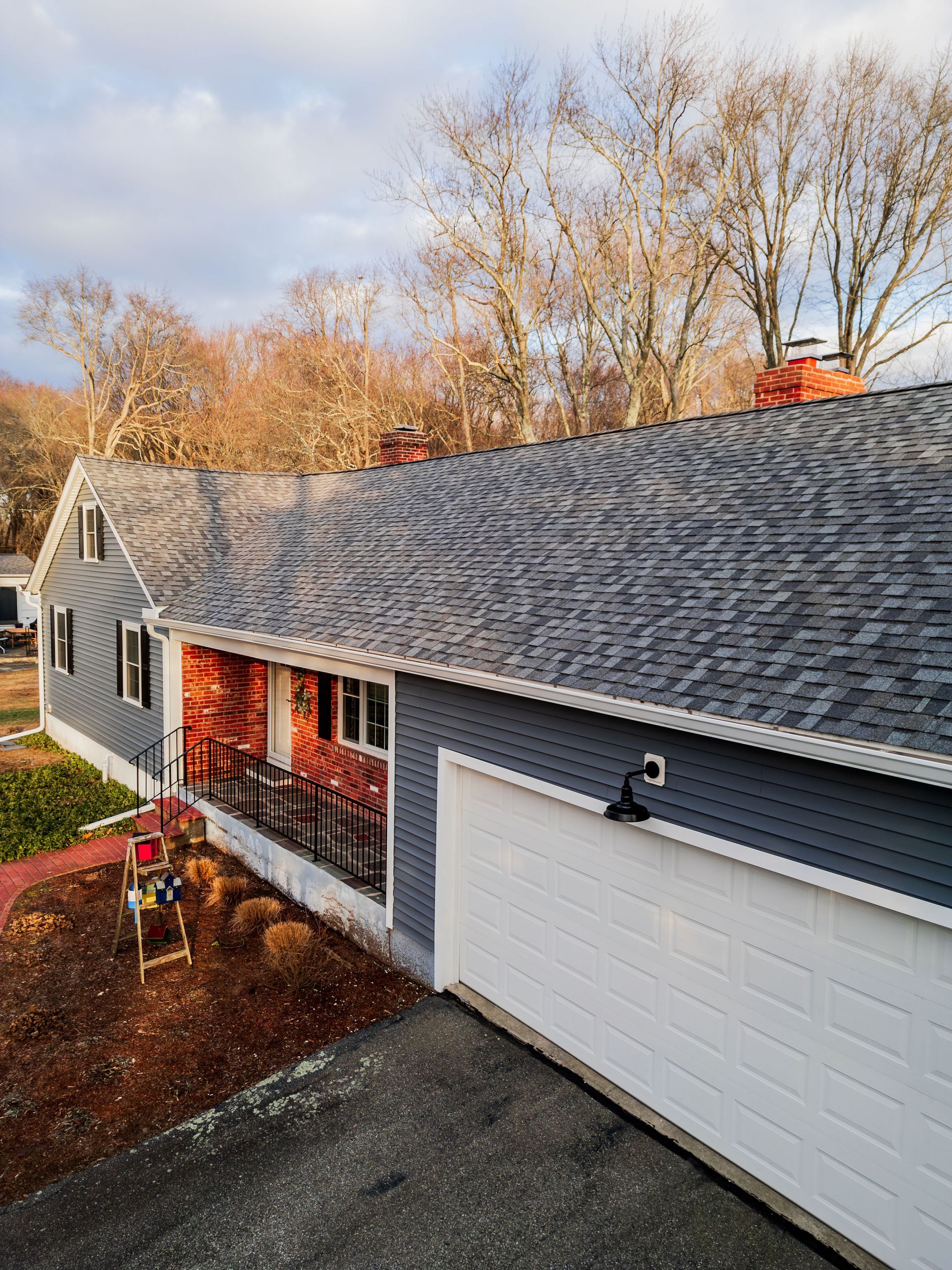 A gray house with a white garage door, red brick entryway, and a cloudy sky.