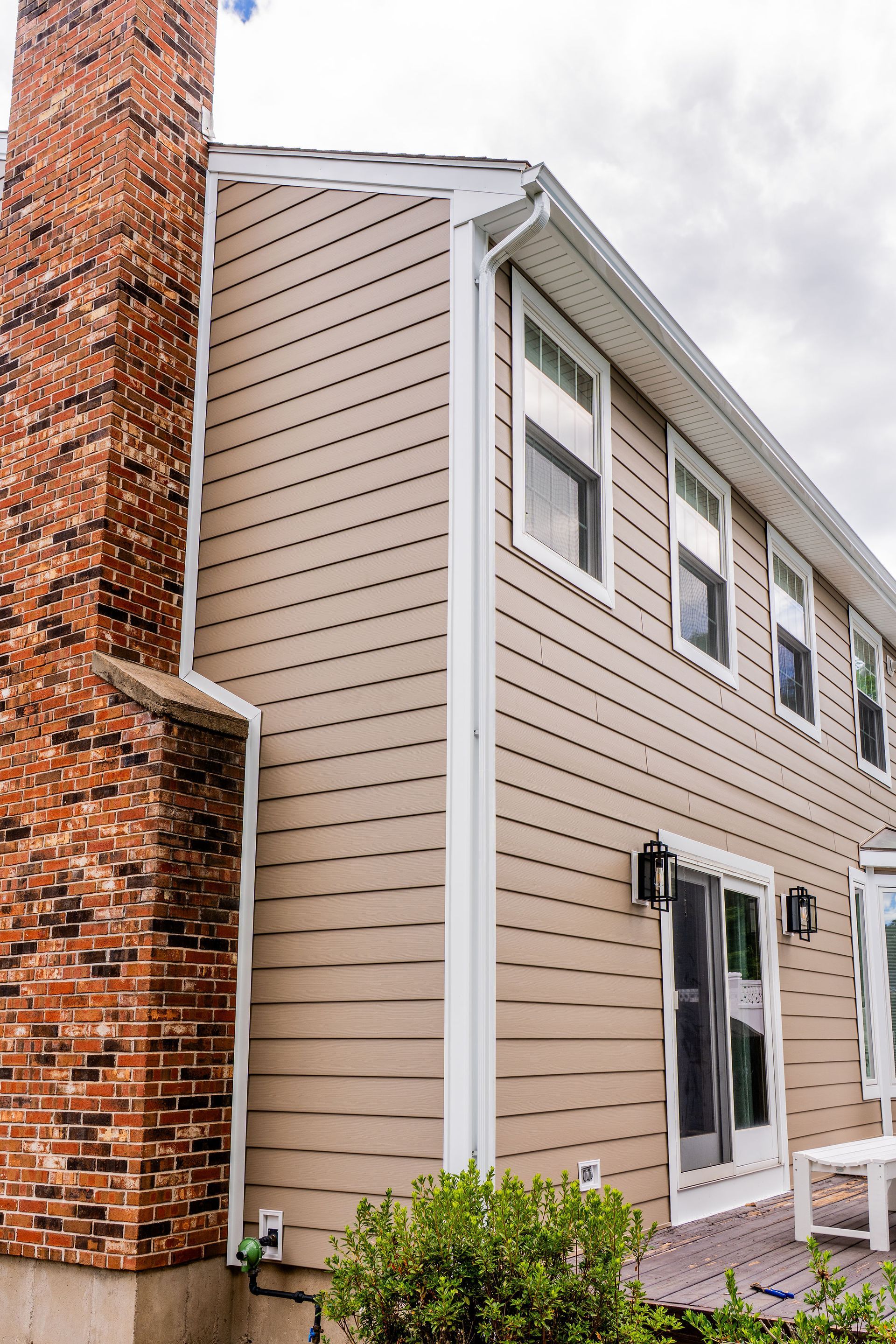 Tan siding on a two-story building with a brick chimney, white trim, and windows.