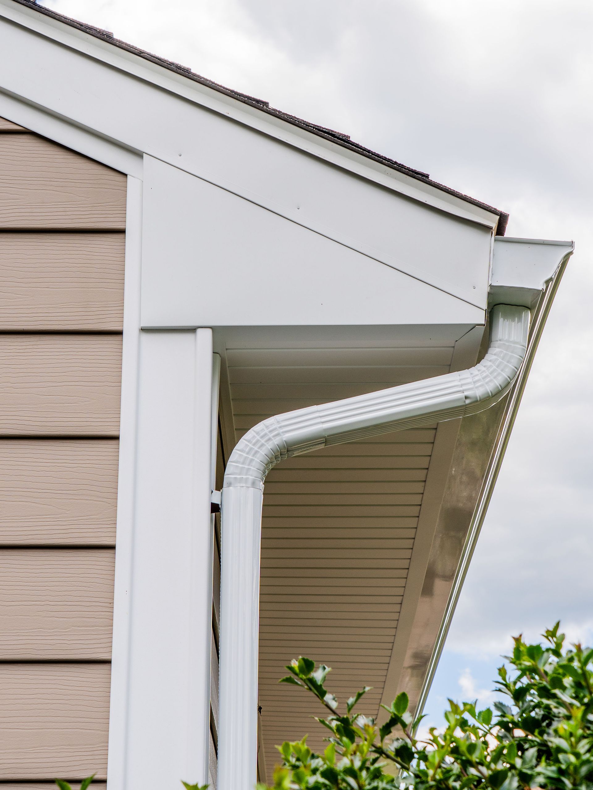 White gutter on a house corner, against beige siding and a blue sky.