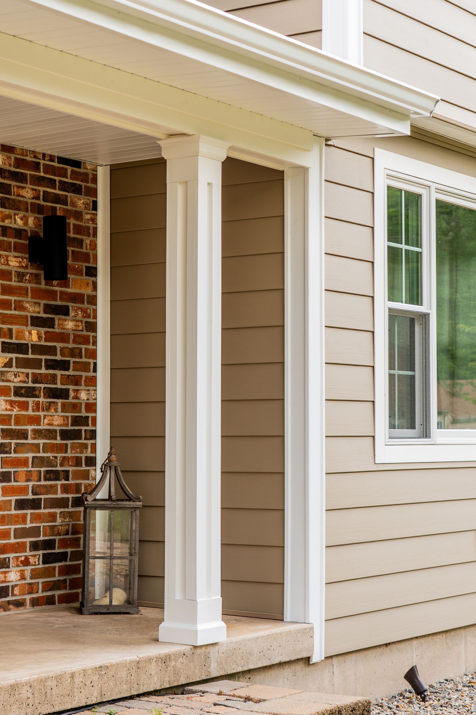 Porch with white columns, brick wall, and lantern on a tan-sided house.