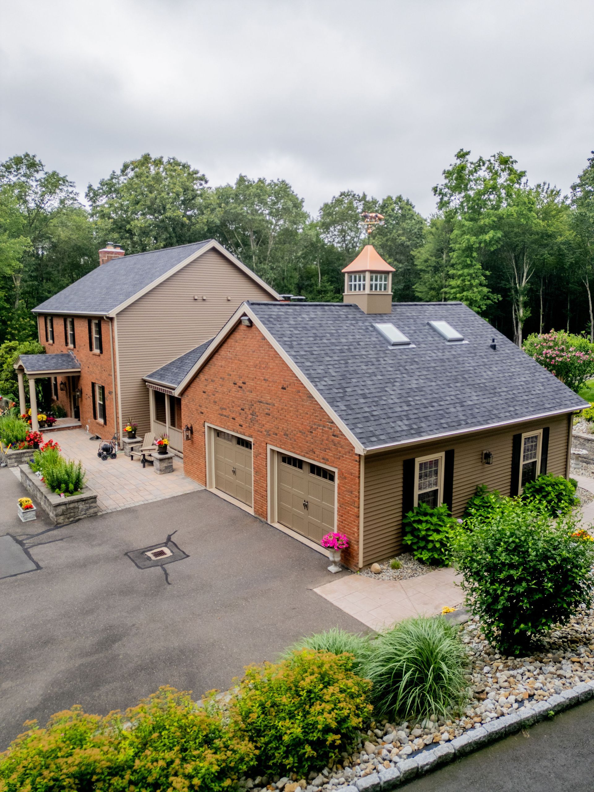 Two-story house with brick garage, surrounded by greenery, and a cloudy sky.