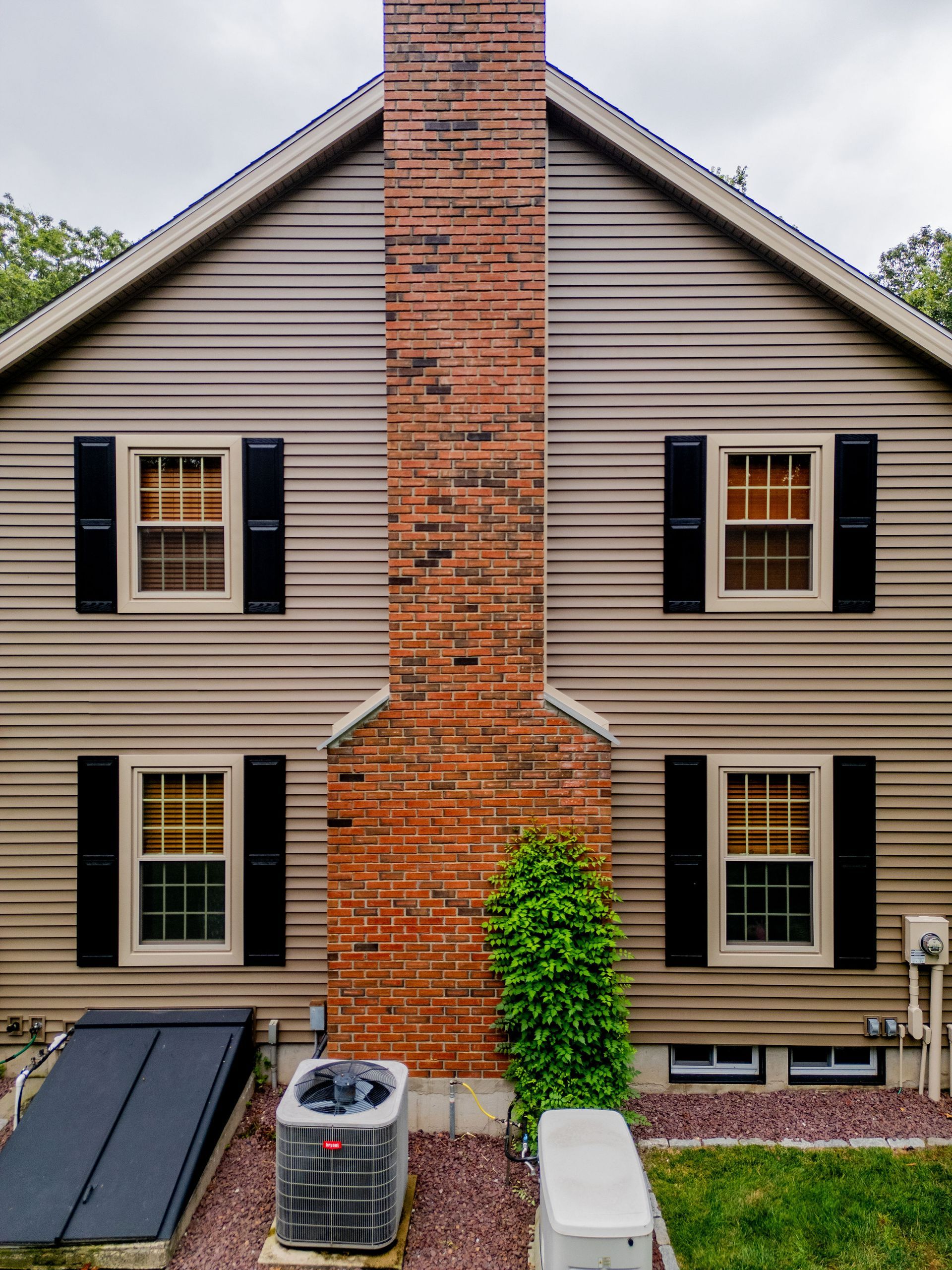 Beige house with brick chimney, four windows with black shutters.