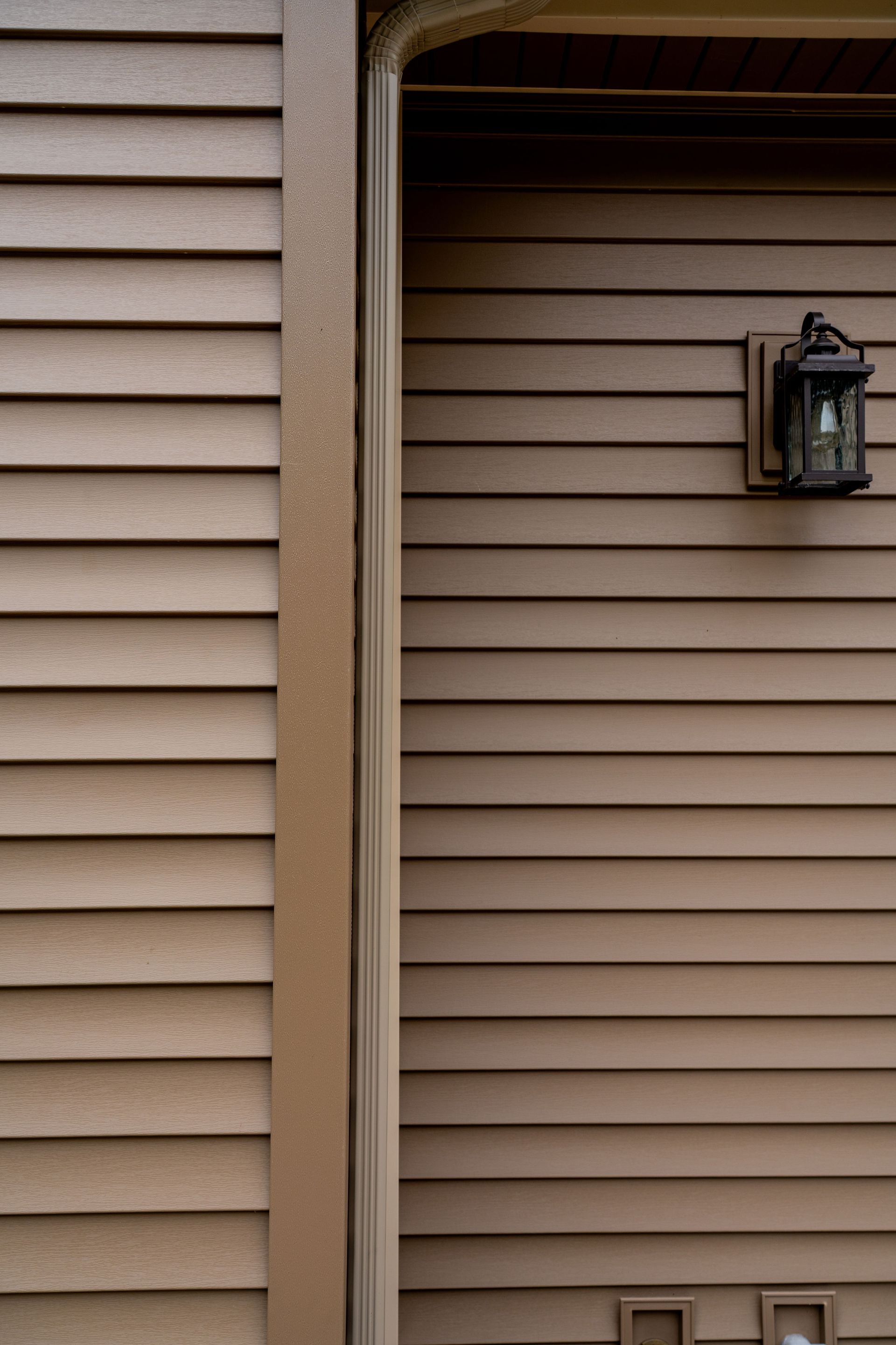 Brown siding with a wall-mounted lantern next to a door frame.