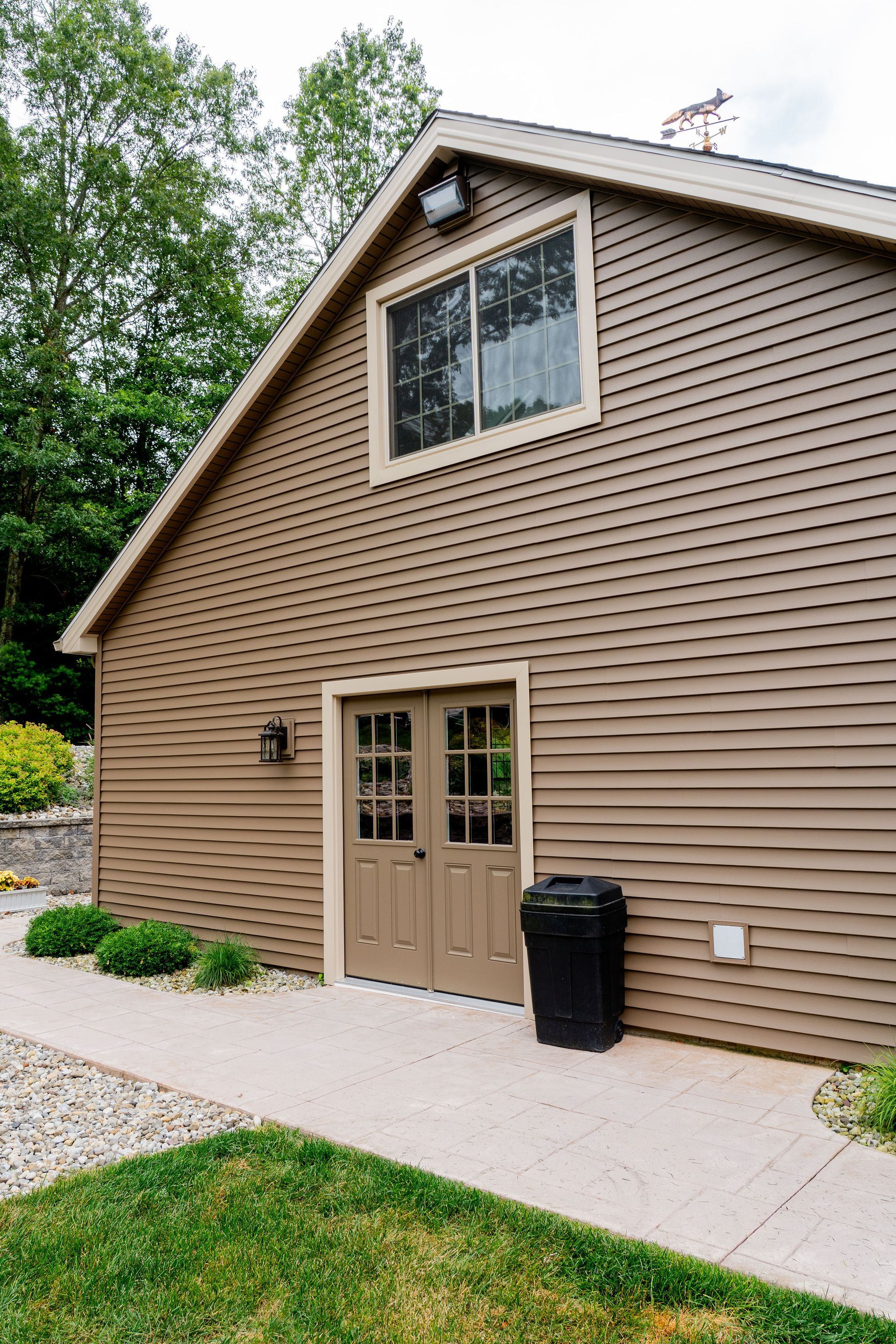 Brown building with double doors, window, and trash can, on a paved path.