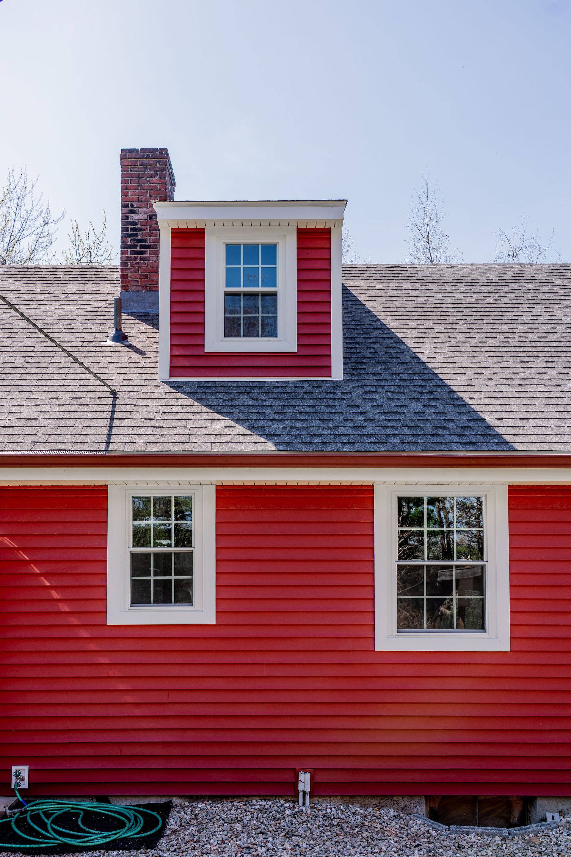 Red house with white-framed windows, dormer, and brick chimney against a blue sky.