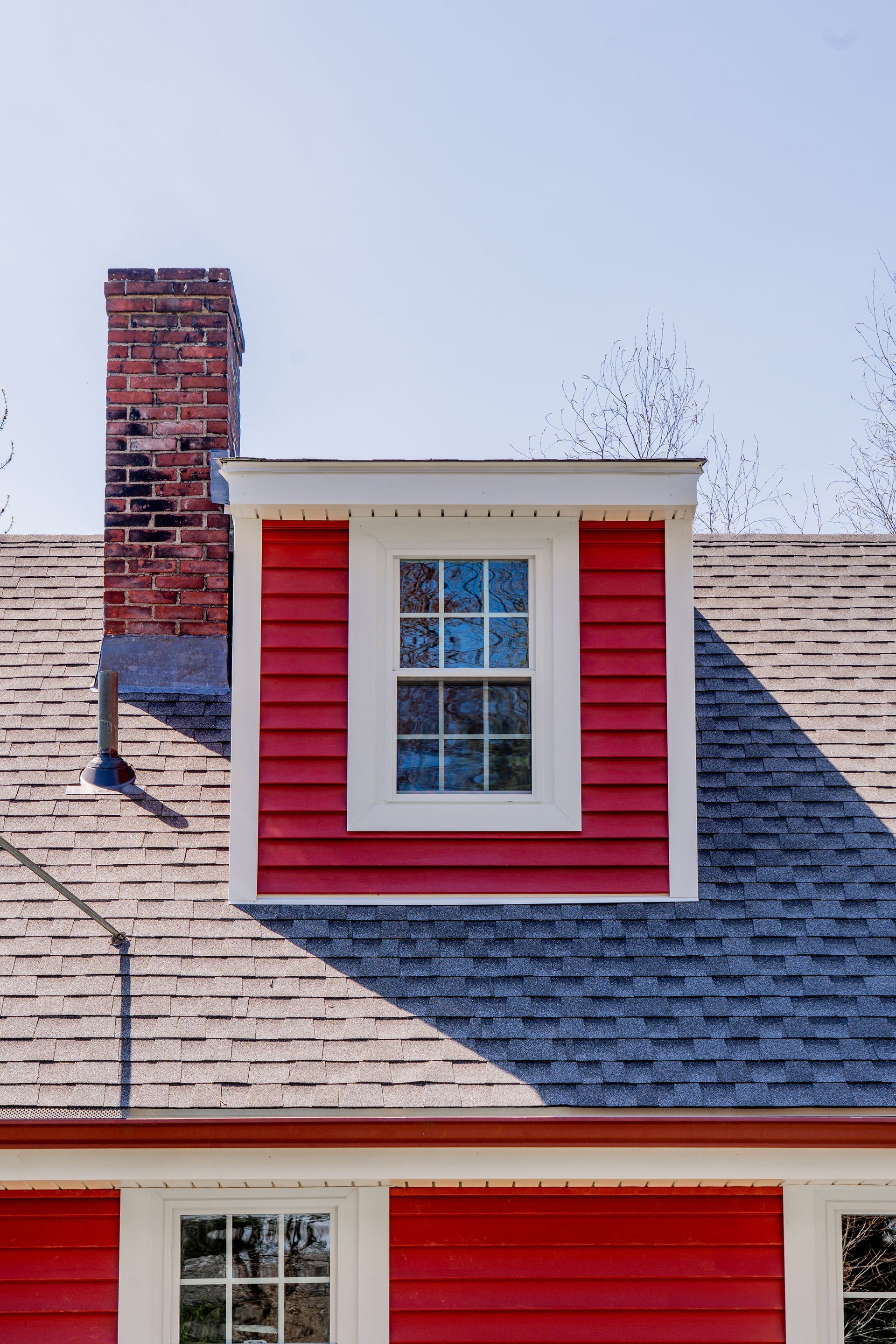 Red dormer window and brick chimney on a gray shingle roof, under a clear blue sky.