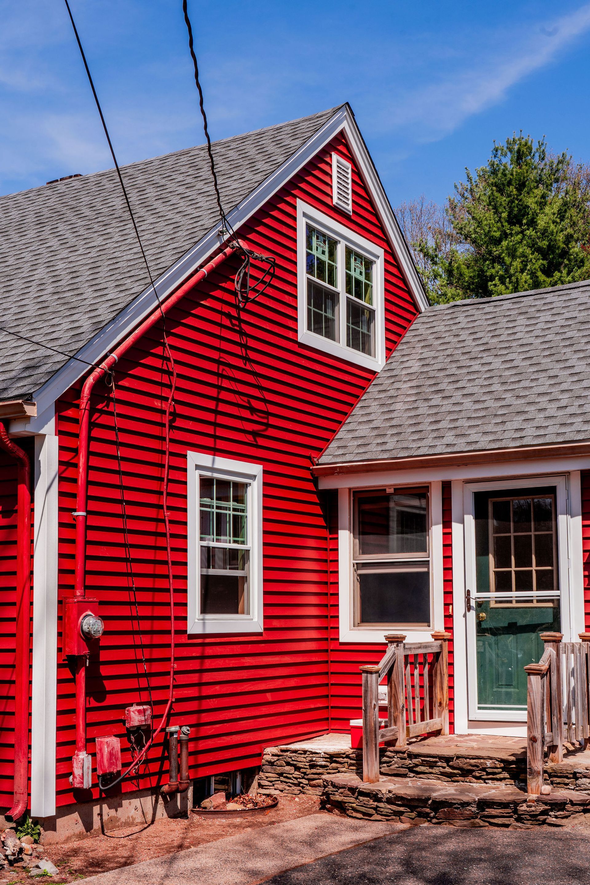 Red house with white trim and gray roof against a blue sky.