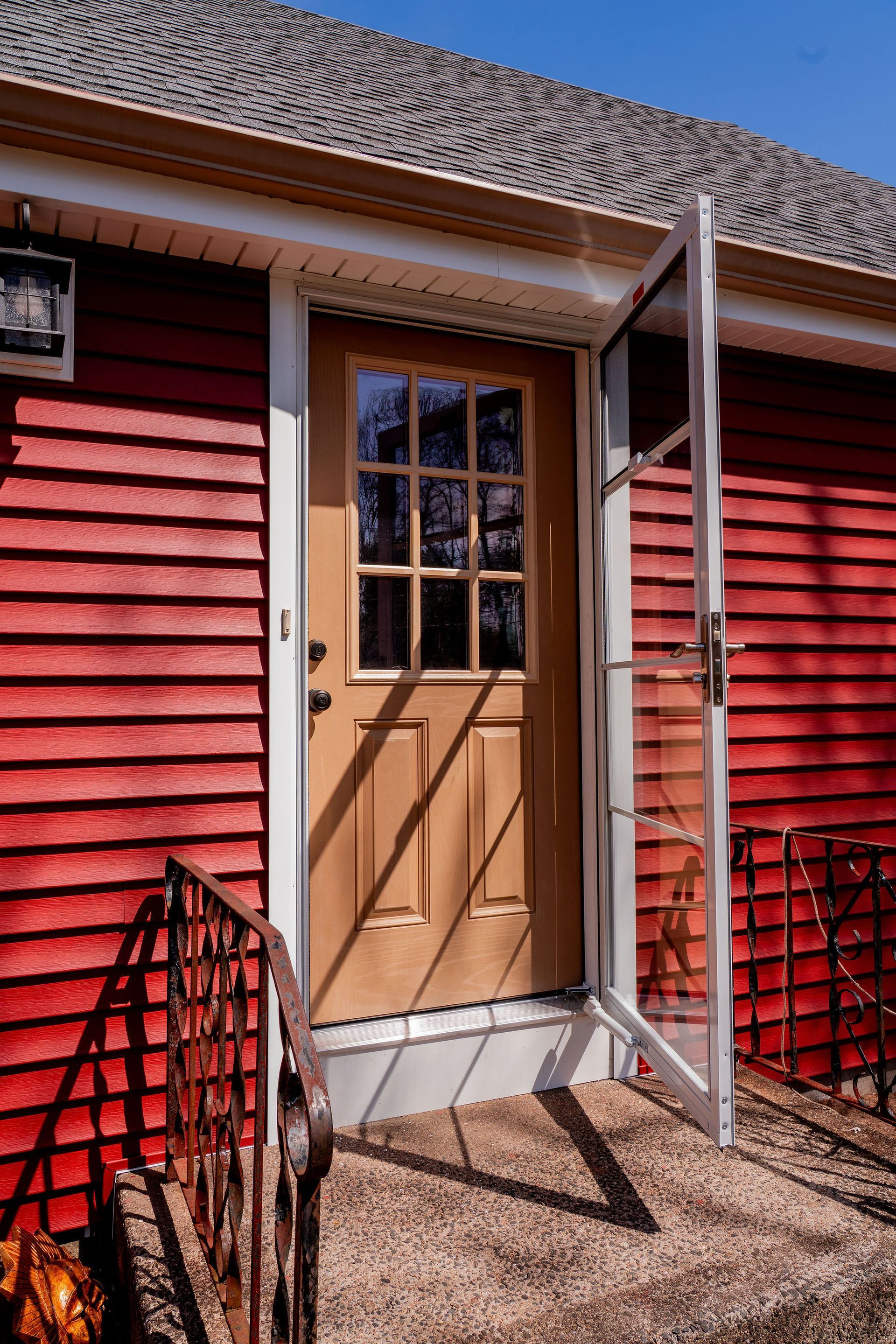 Red building with light brown door and open screen door; sunny day.