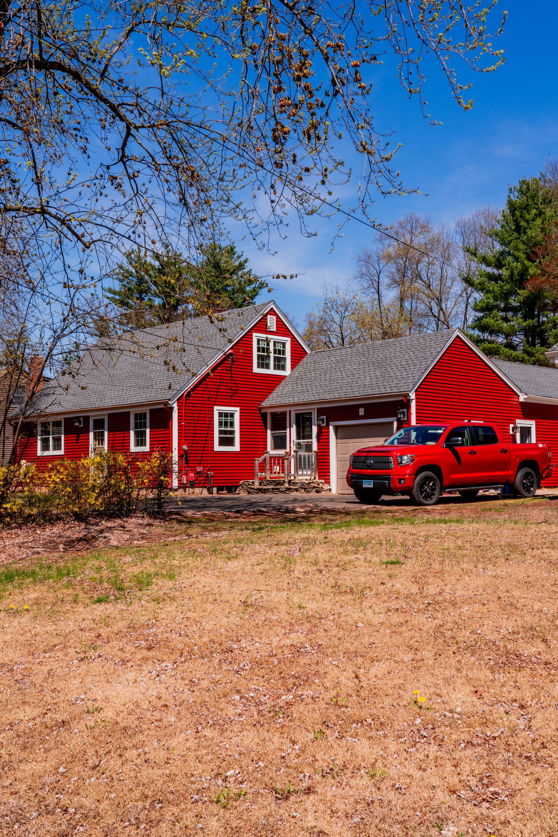 Red house with a red truck in the driveway under a blue sky, trees in the background.