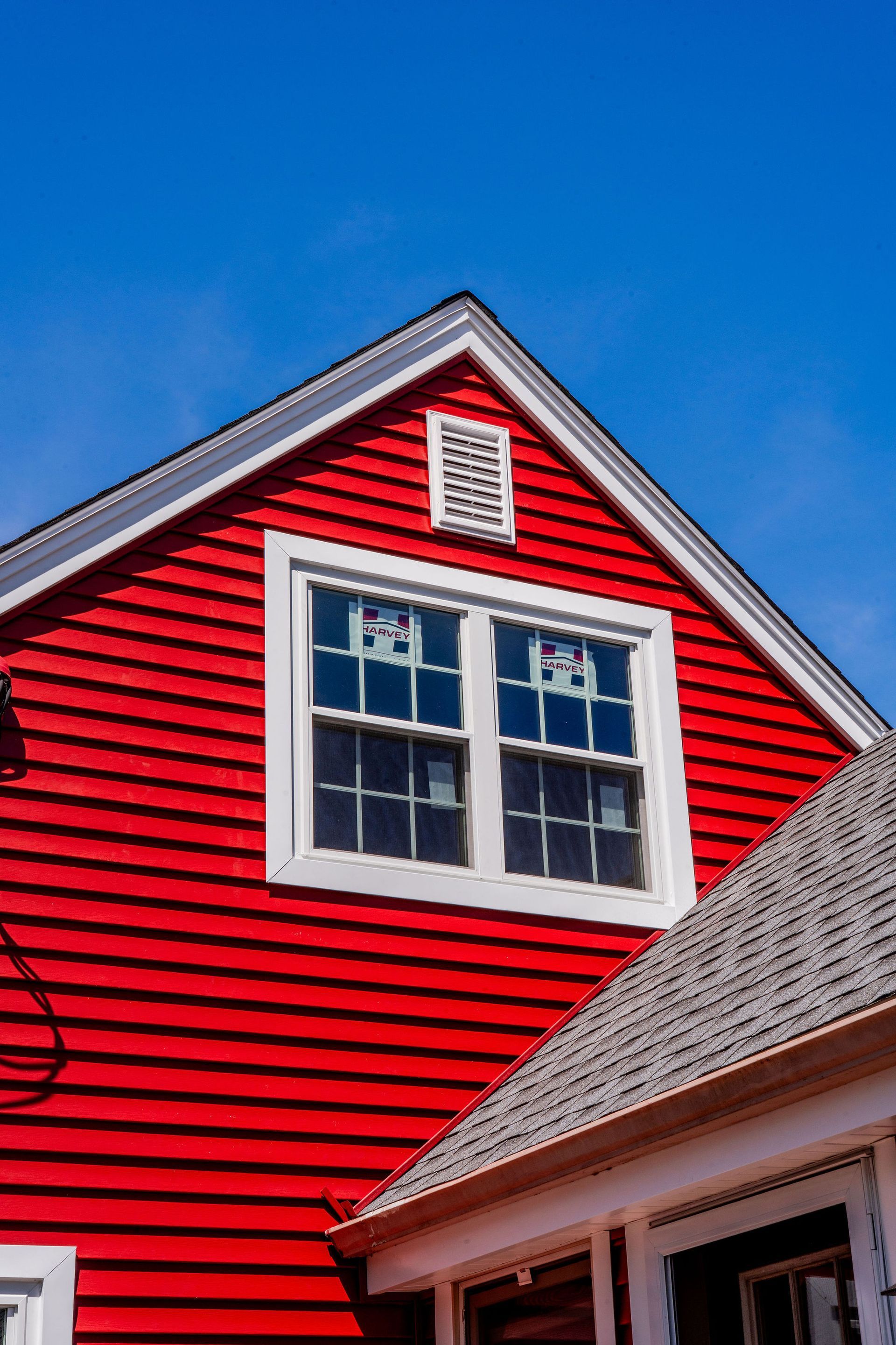 Red-sided building with white-framed windows and a small, white vent against a bright blue sky.