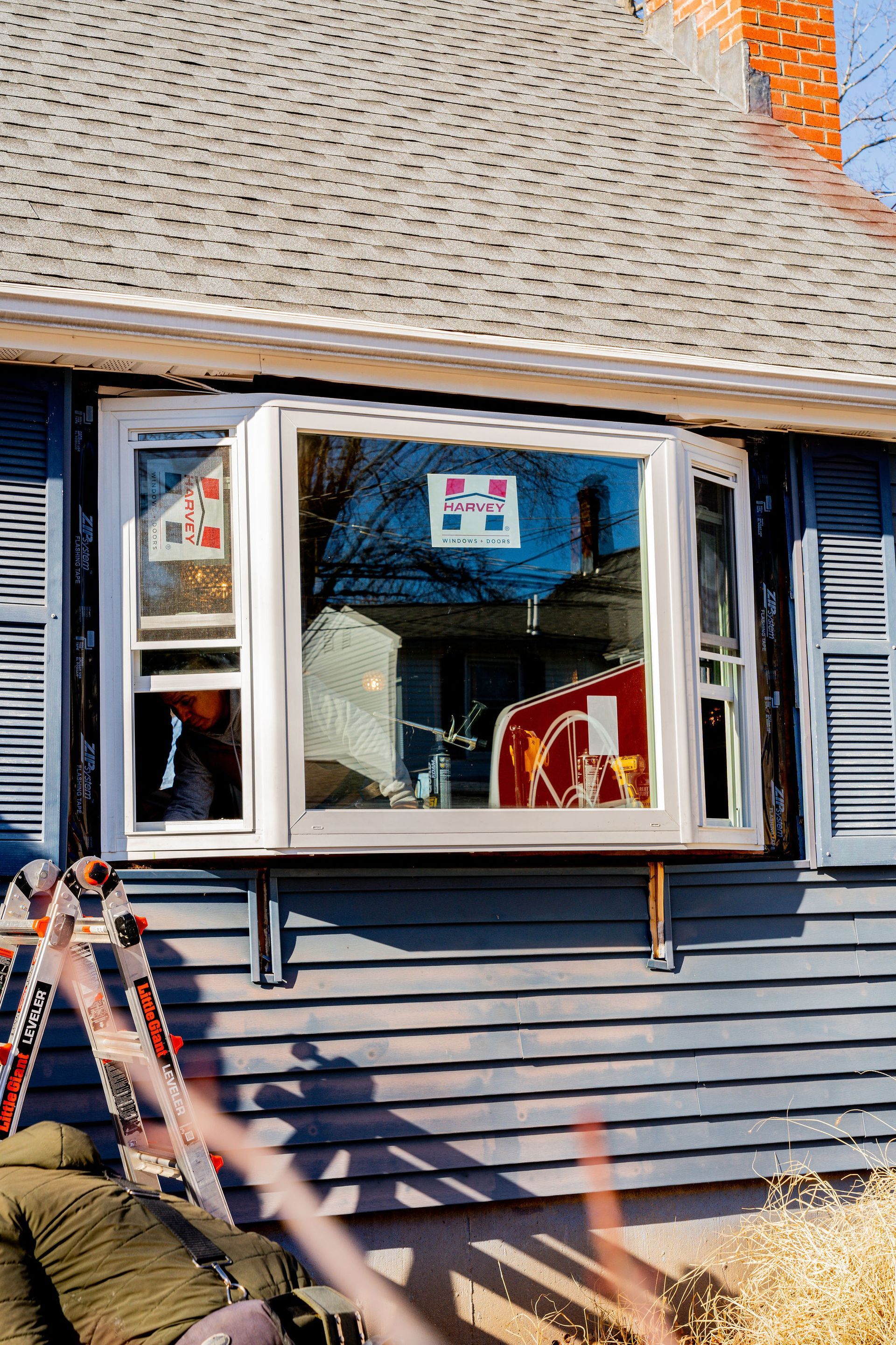 Bay window on a blue house with white trim. A ladder is leaning against the building.