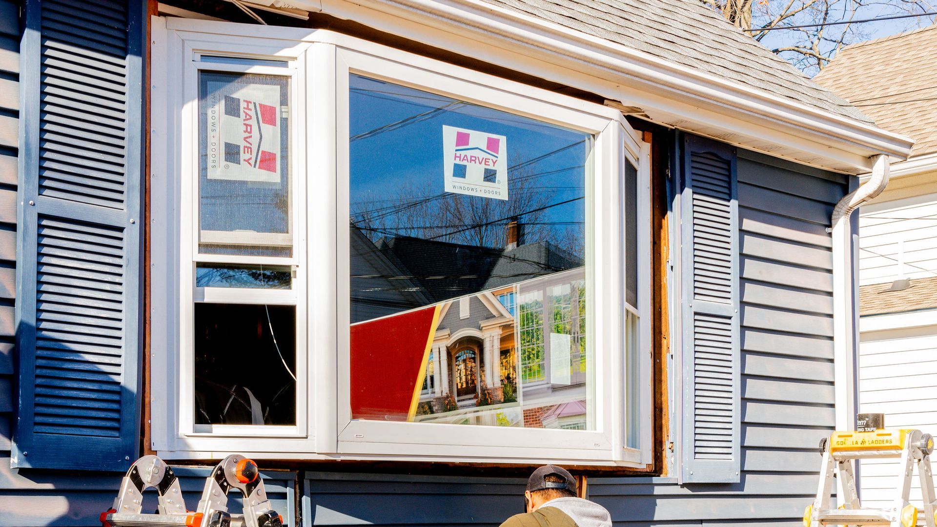 A man is installing a bay window on the side of a house.