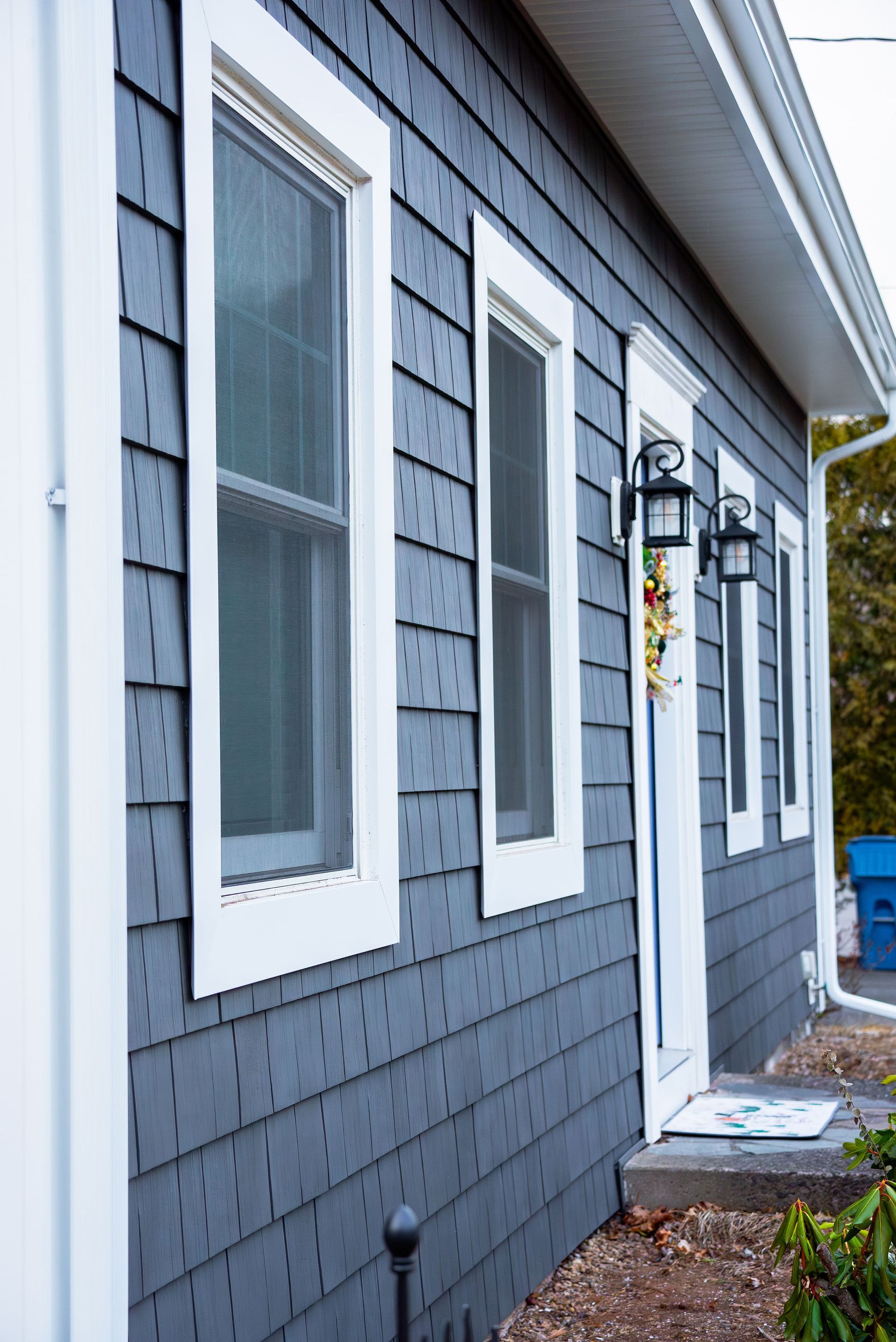 Dark gray shingle-sided house with white trim, windows, and entry door.