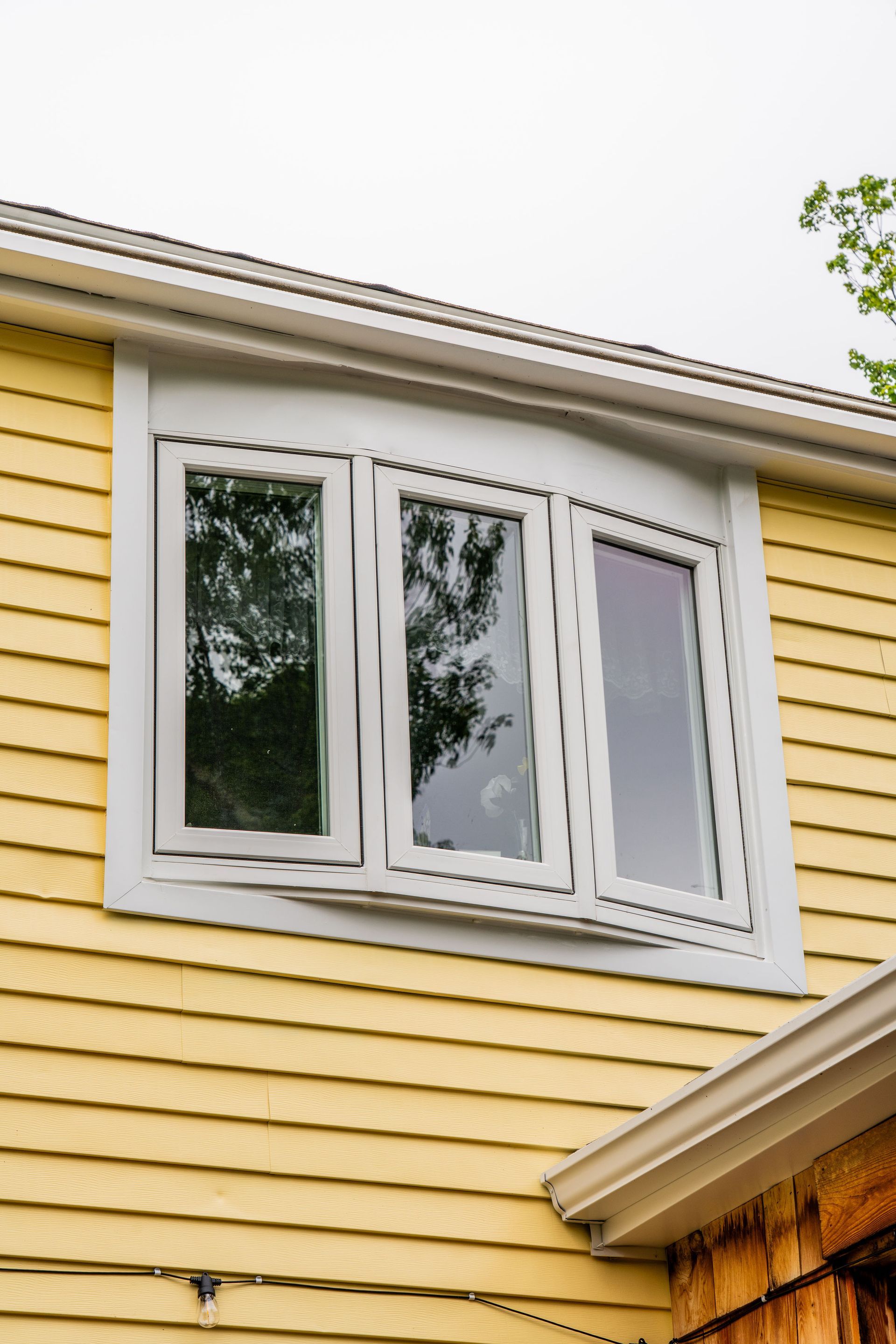 Bow window with three panes set in a gray frame on a yellow house with gray trim.