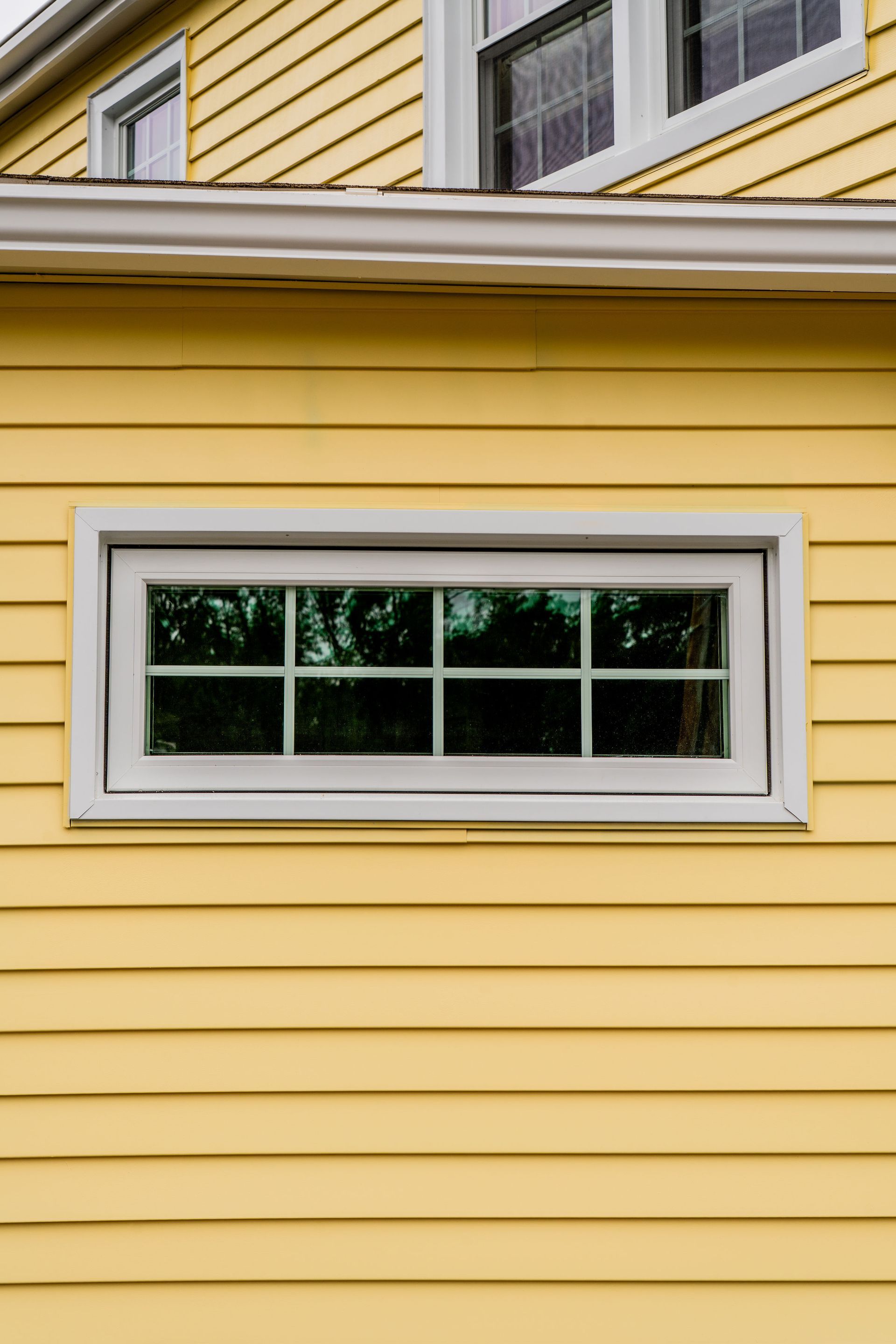 Yellow house siding with a rectangular window and white trim.