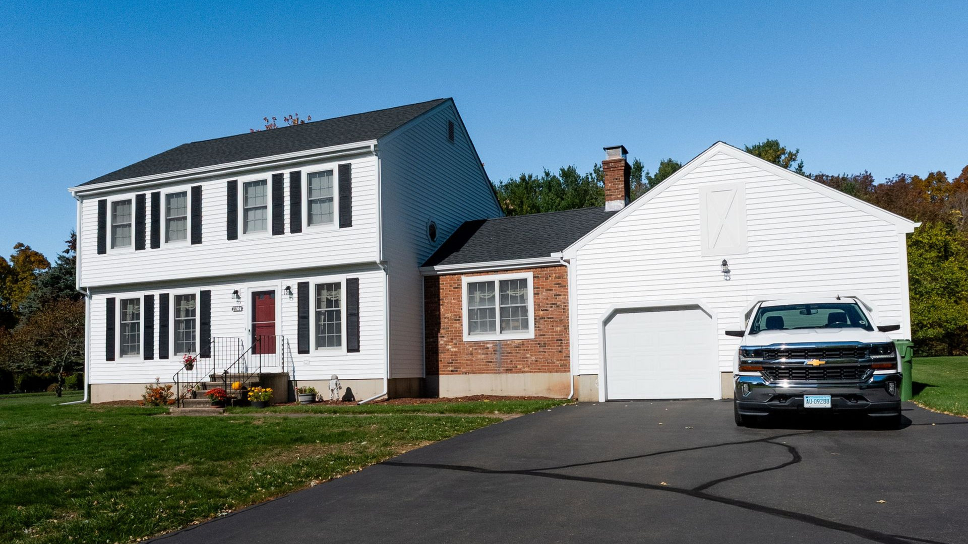 Two-story white house with black shutters, attached garage, and black asphalt driveway; a truck is parked in front.