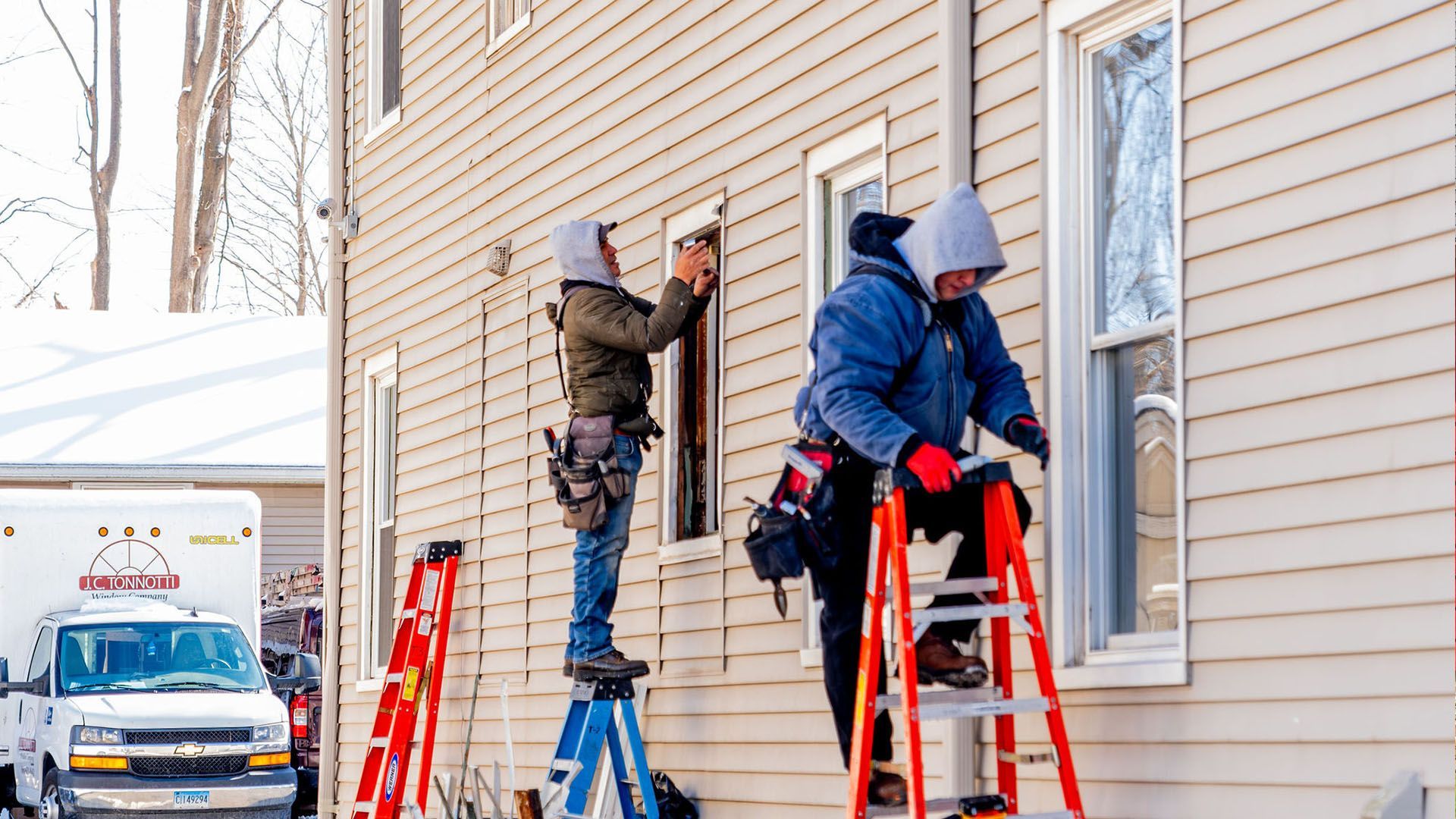 Two men are working on a window on the side of a house.